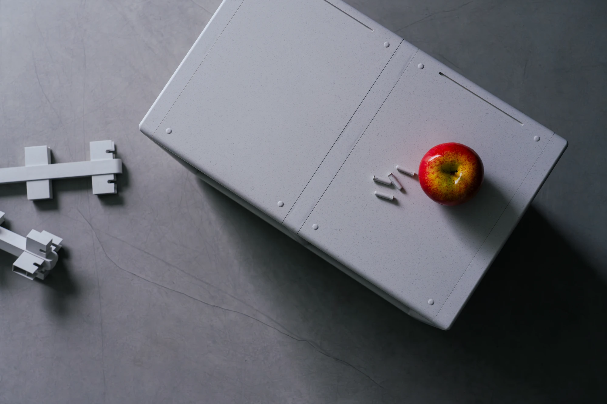 reol: Modular Narratives in Recycled Plastic by reol — A single small reol unit in profile against a grey concrete floor: the open face visible, corner brackets exposed, two white mini-figures placed near it for scale.