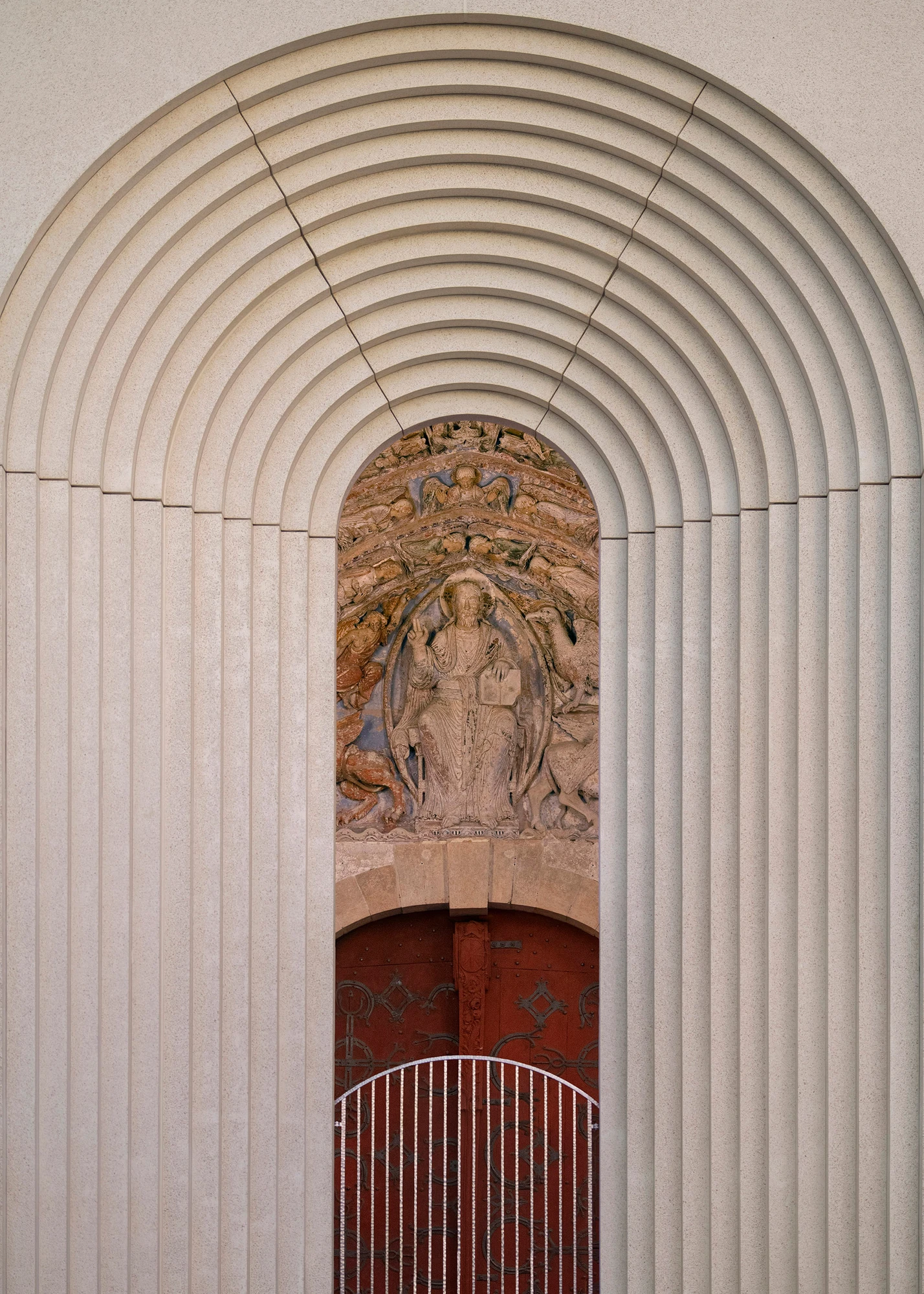 Angers Cathedral Entrance by Kengo Kuma and Associates — Close detail of a single arch: concentric concrete archivolts frame a carved tympanum, the polychrome figures of the 17th-century relief visible beneath ribbed concrete bands.