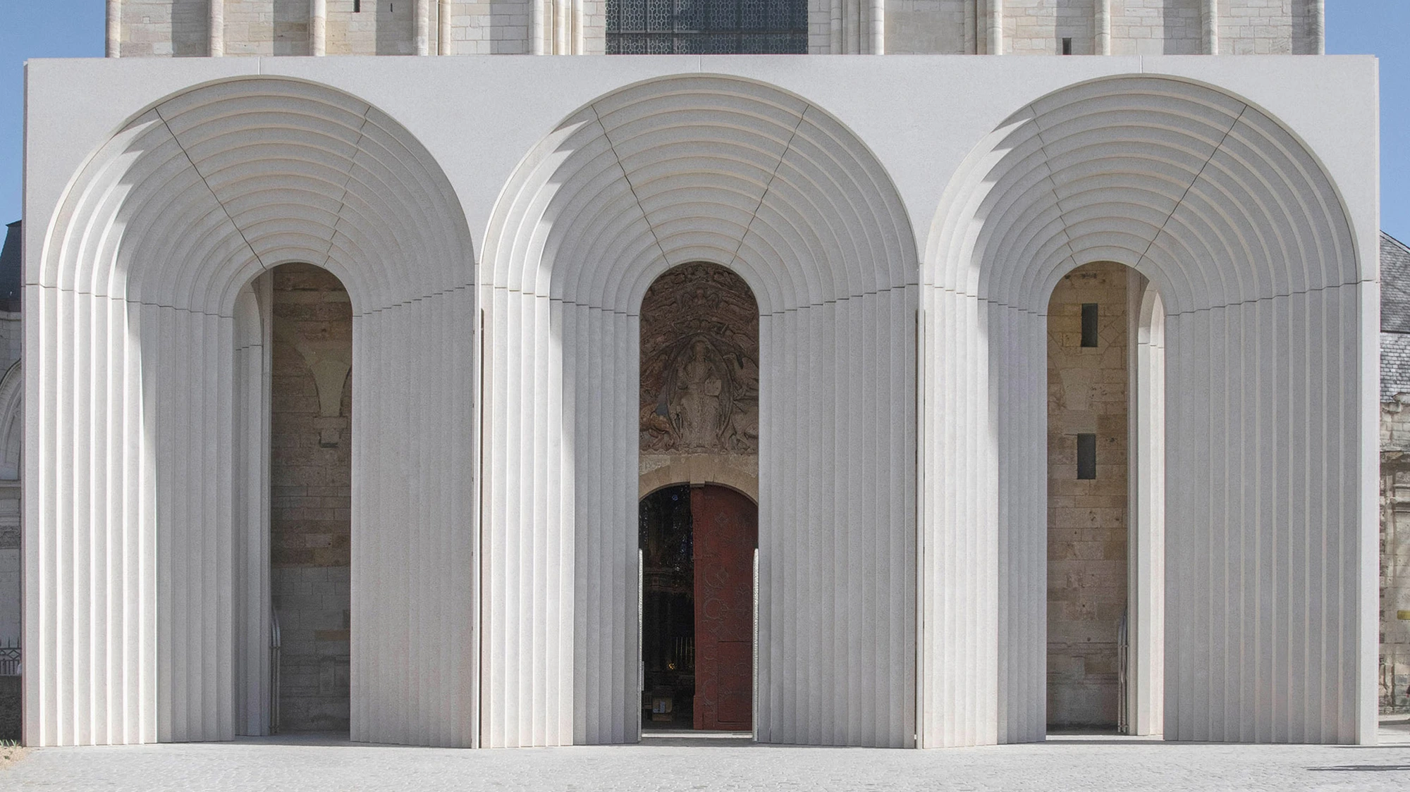 Angers Cathedral Entrance by Kengo Kuma and Associates — Three deeply ribbed concrete arches frame the medieval portal of Angers Cathedral, their pale off-white surface precisely cast with repeating archivolt bands.