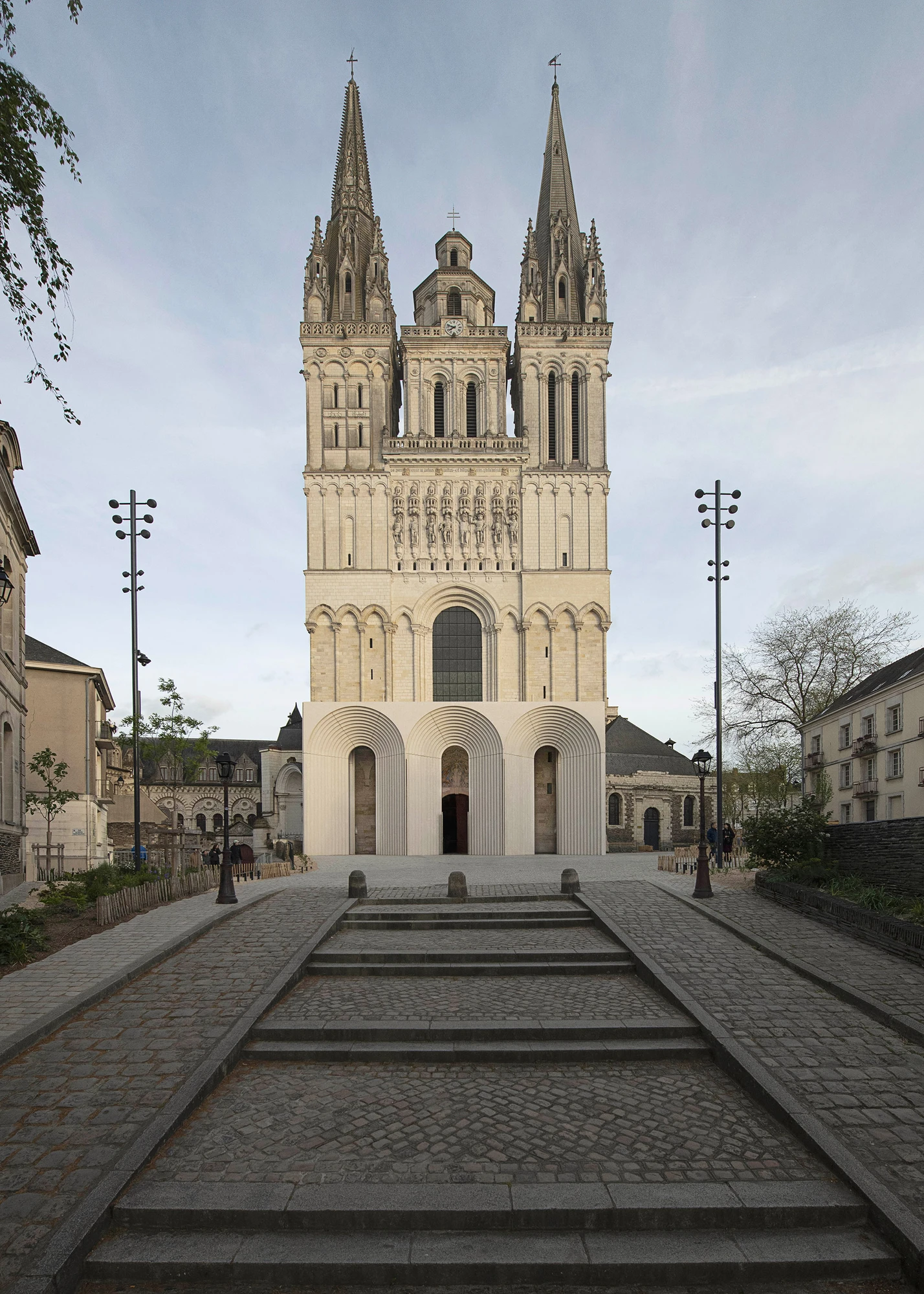 Angers Cathedral Entrance by Kengo Kuma and Associates — Full frontal view of the cathedral: the new low horizontal concrete entrance sits against the Gothic twin-tower facade, its white mass reading as a separate body at the building's base.