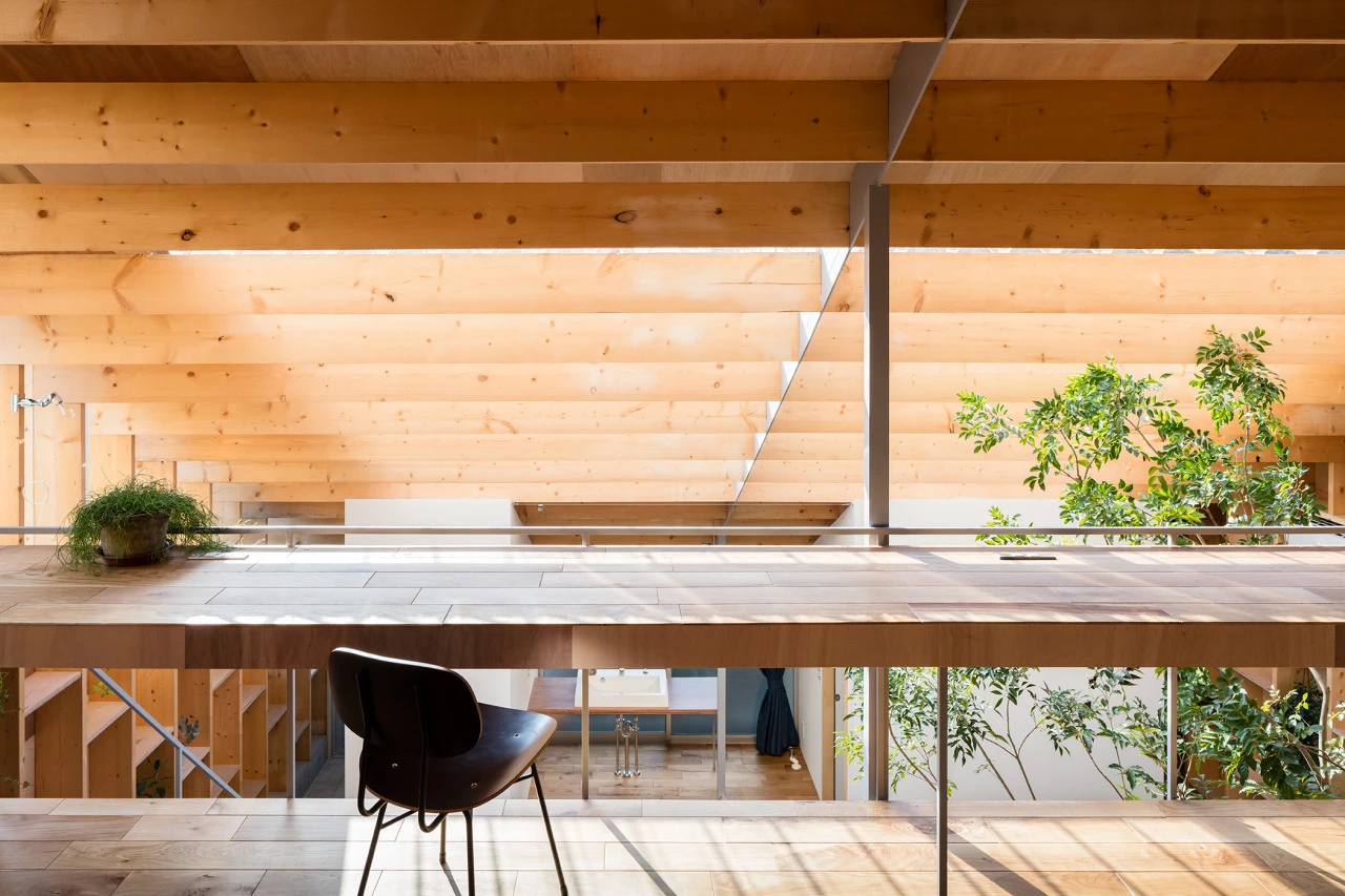 Detached House by mA Style Architects, photographed by Kai Nakamura — A close desk view: a single black chair faces a long wood surface, plants placed on shelves, the courtyard glazing behind as a bright backdrop.