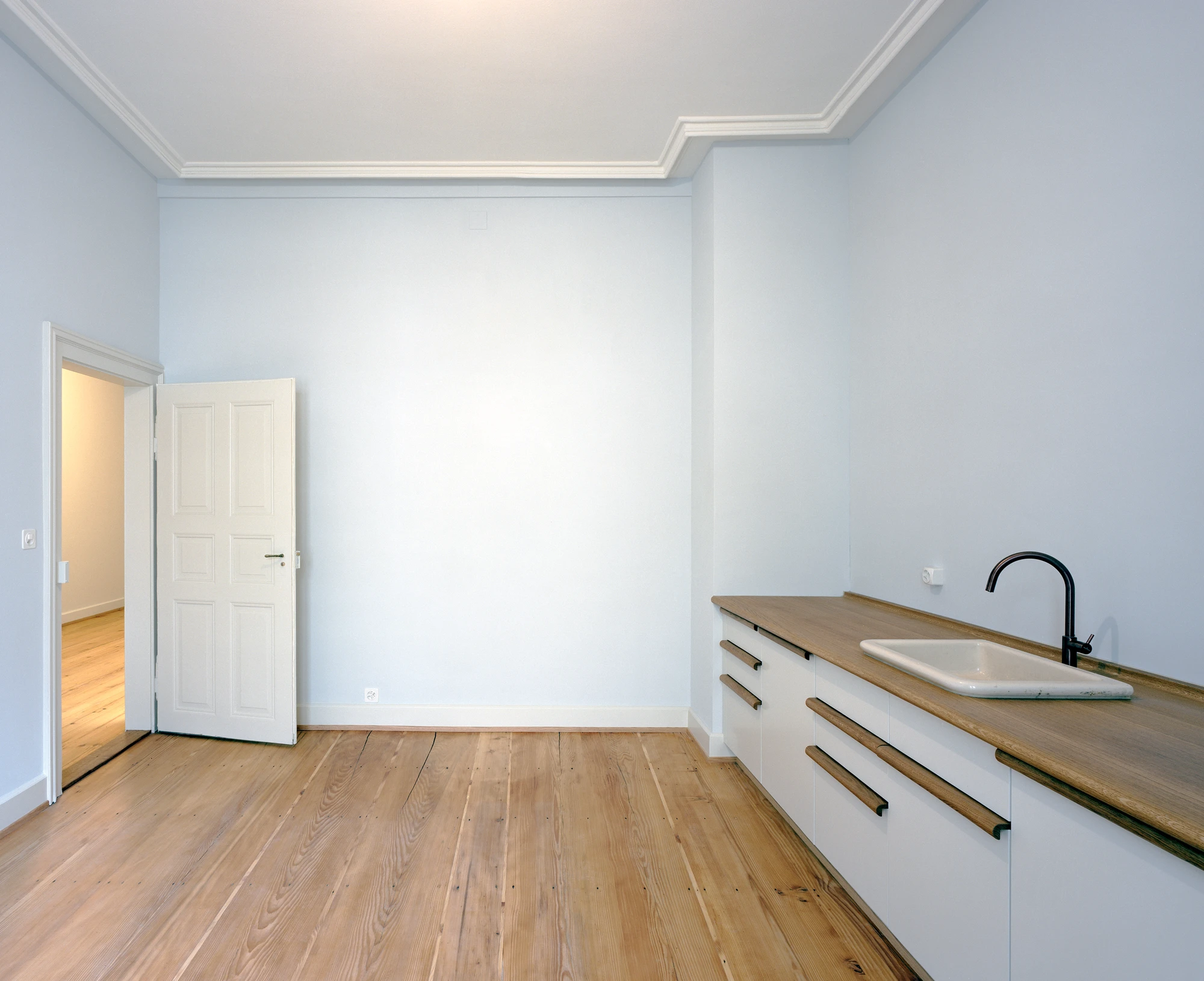Ehemaliges Pfarrhaus Elisabethenstrasse by Vecsey Schmidt Architekten, photographed by Barbara Buhler — Restored bel etage room with pale blue-grey walls, pine floorboards, and a modern white kitchen with oak counter.
