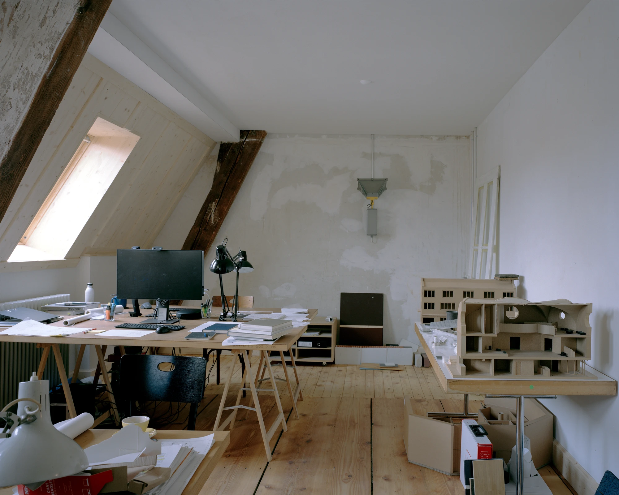 Ehemaliges Pfarrhaus Elisabethenstrasse by Vecsey Schmidt Architekten, photographed by Barbara Buhler — Active working studio under the attic pitch, trestle desk with drawings, roof window, and a detailed scale model.