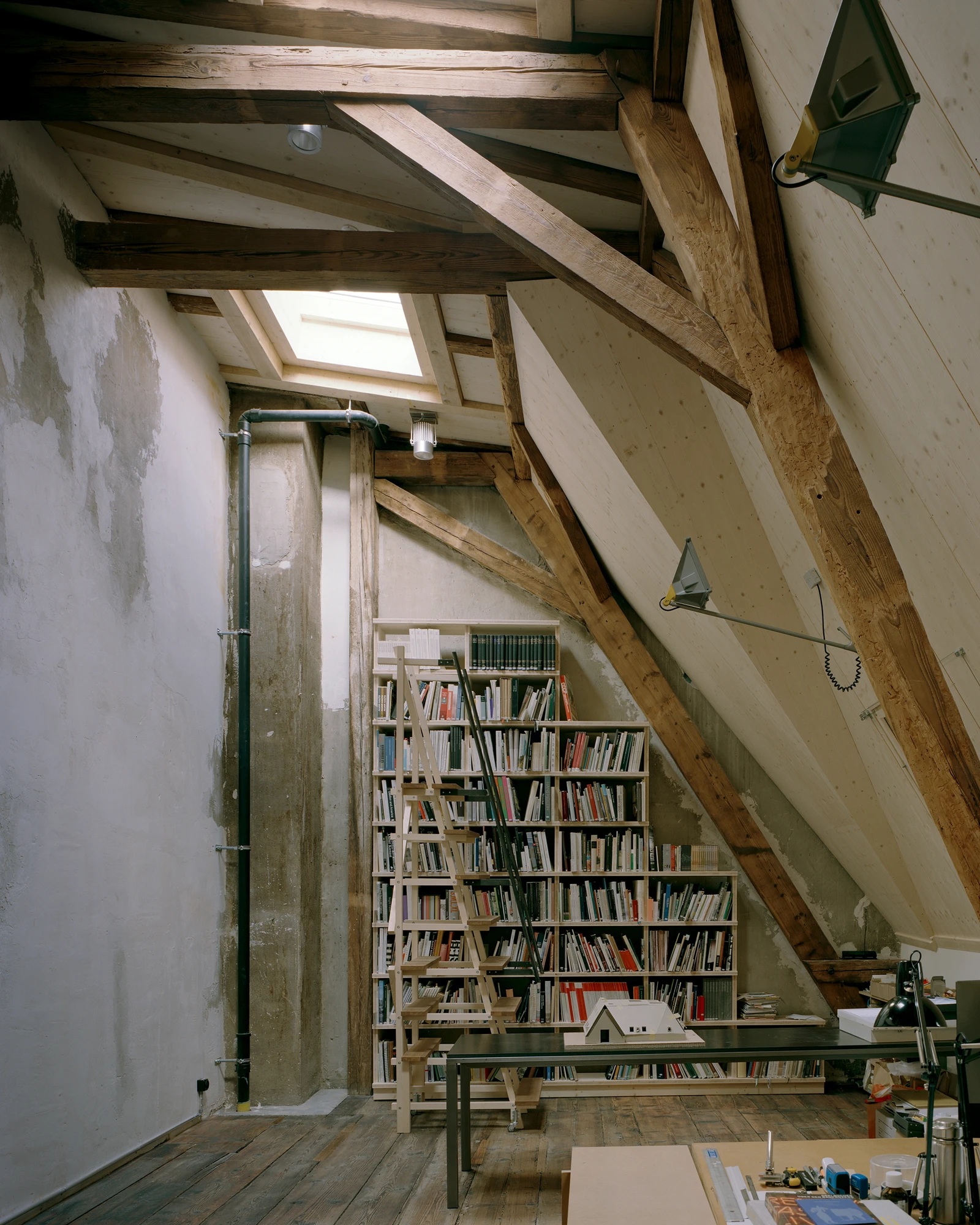Ehemaliges Pfarrhaus Elisabethenstrasse by Vecsey Schmidt Architekten, photographed by Barbara Buhler — Attic library with heavy oak trusses, bookshelves filling the triangular void, zenithal skylight, and raw concrete column.