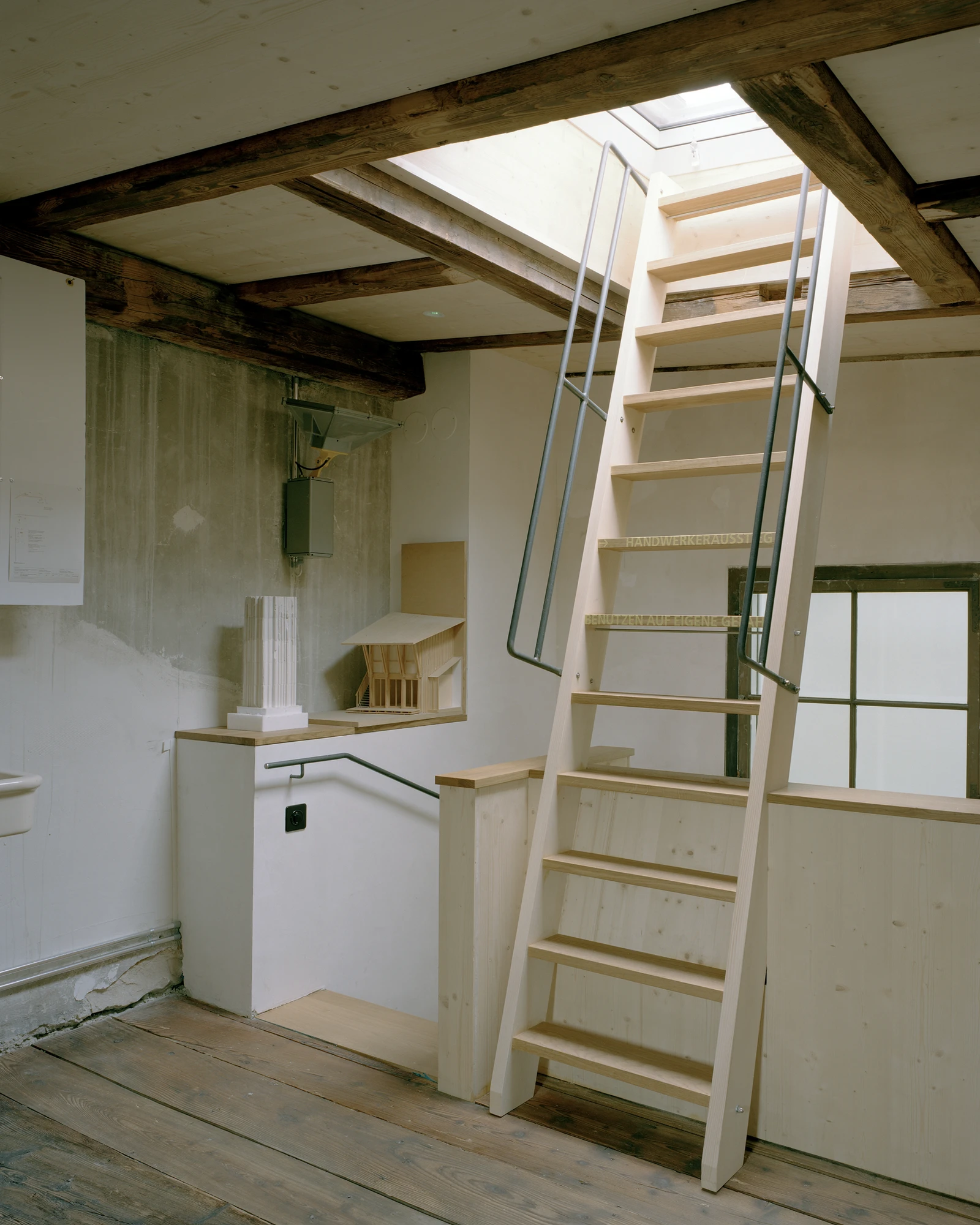 Ehemaliges Pfarrhaus Elisabethenstrasse by Vecsey Schmidt Architekten, photographed by Barbara Buhler — Attic conversion showing exposed ancient timber beams, paired skylights above a ship's ladder stair with steel handrail.