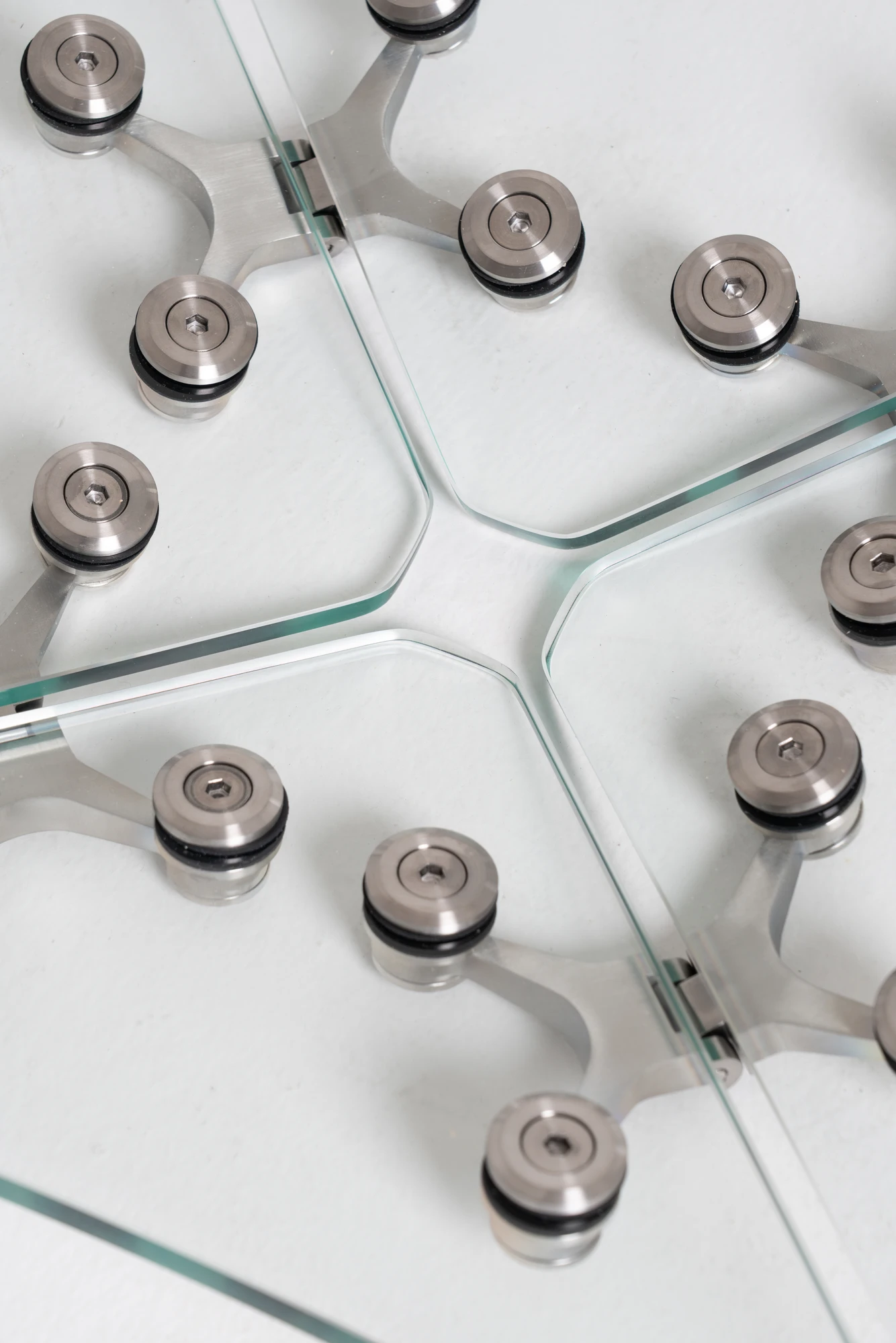 Ferric Glass by Tino Seubert, photographed by Piercarlo Quecchia, DSL Studio — Table lamp silhouette on white: lit internally, the hexagonal glass panels diffuse the bulb glow, shadow pattern of spider hinges projected below.