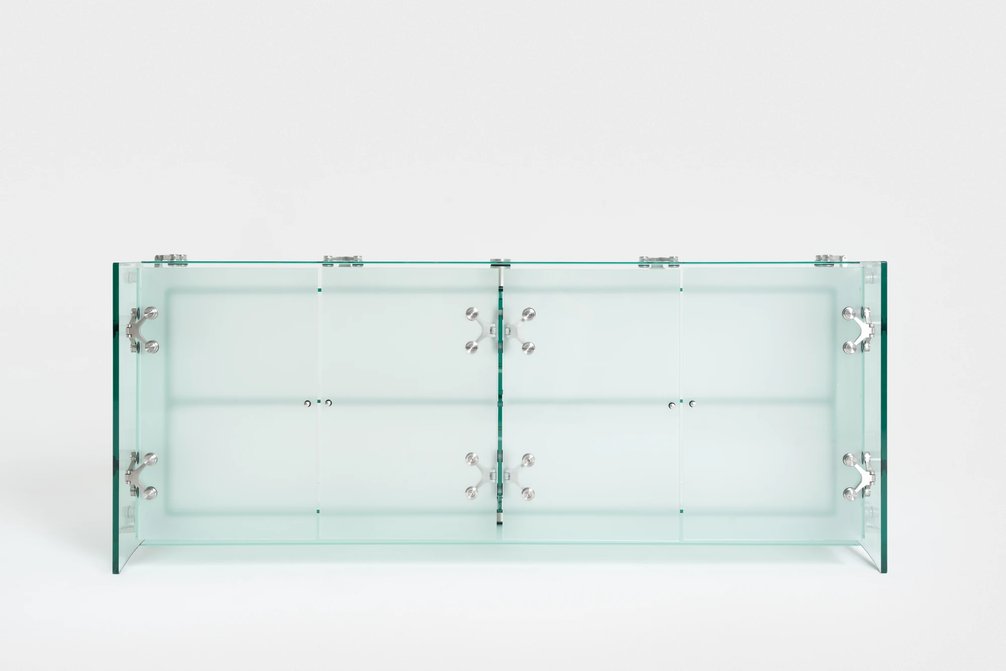 Ferric Glass by Tino Seubert, photographed by Piercarlo Quecchia, DSL Studio — Macro detail of a spider hinge at a glass-to-glass junction: four-arm stainless steel fitting, the deep teal glass edge section in the centre, everything machined to tolerance.