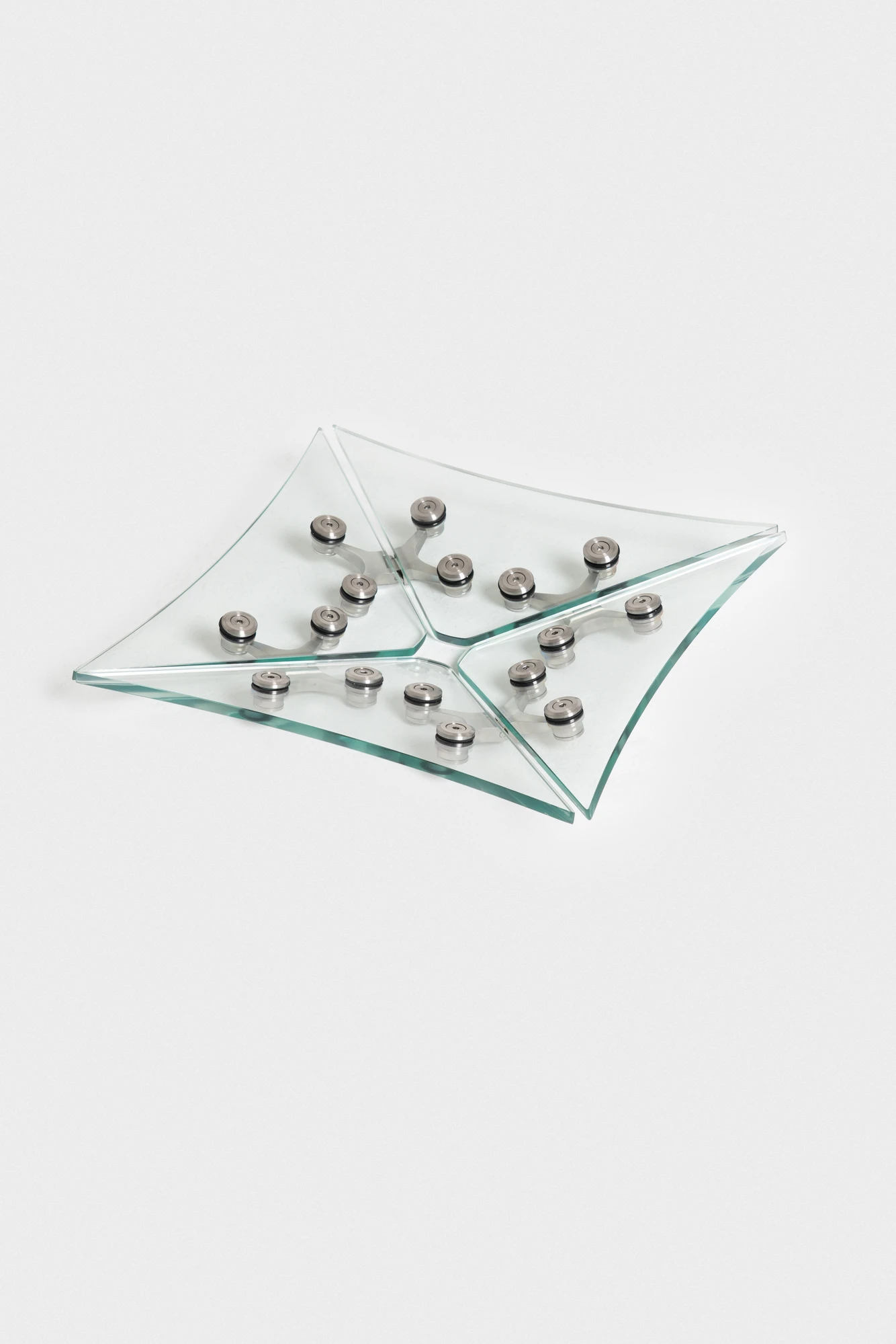 Ferric Glass by Tino Seubert, photographed by Piercarlo Quecchia, DSL Studio — Studio detail: frosted high-iron glass panel surface showing the green tint at the cut edge, four stainless spider-hinge arms radiating from a central boss.