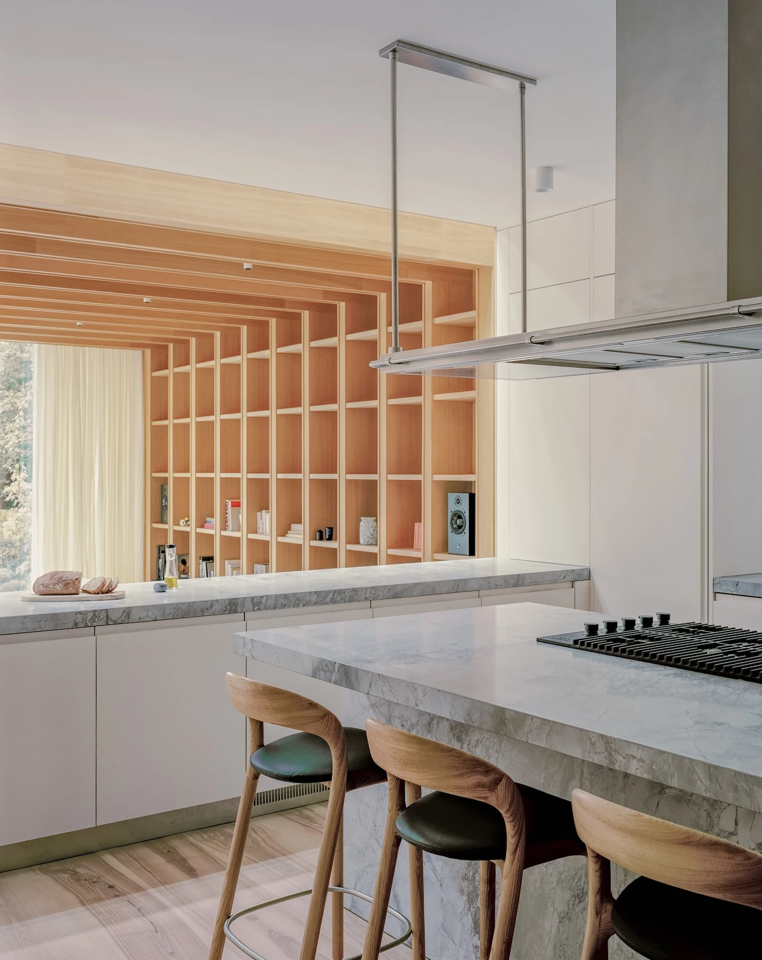 Panoramic House by MATA Architects, photographed by Nick Dearden — Dining area in the original house: oak panelled walls, an inset fireplace with fire burning, long oak dining table and Danish chairs, kitchen alcove behind in stainless steel.