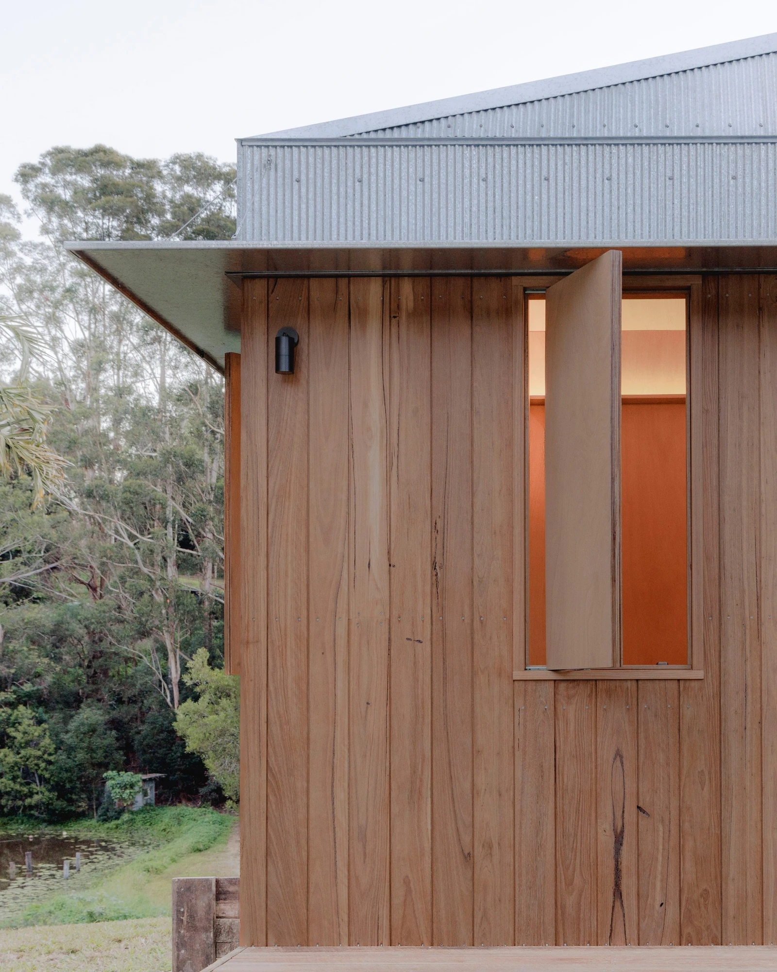 The Oculus by Hayley Pryor — At dusk: the large sliding door panel is open and the interior banquette is lit amber, a pendant light glowing above the circular table.