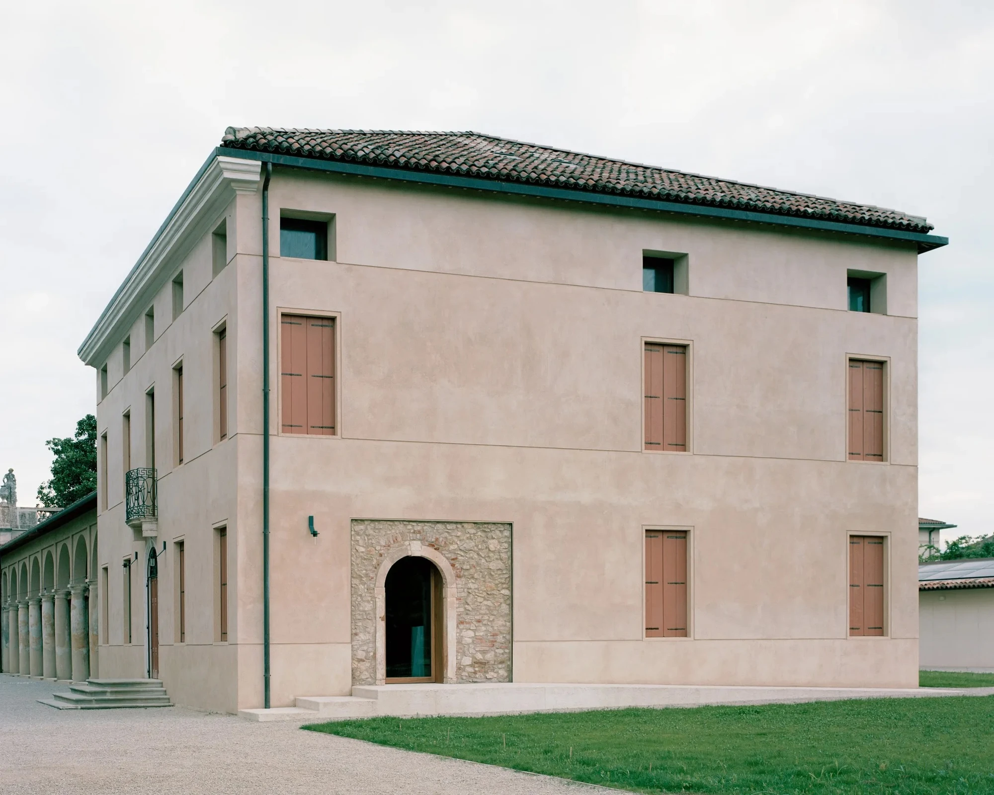 Vis-à-vis Restoration of Villa Doná and Barchessa by RigonSimonetti, photographed by Rory Gardiner, Alberto Sinigaglia — Barchessa colonnade close-up: Tuscan columns with arched bays filled by tall glass panels with bronze-frame sliding doors, the…