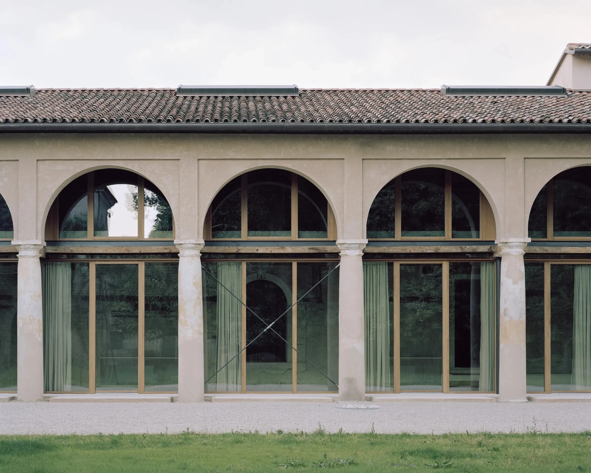 Vis-à-vis Restoration of Villa Doná and Barchessa by RigonSimonetti, photographed by Rory Gardiner, Alberto Sinigaglia — Annex side elevation: rendered white concrete plane meeting the terracotta pitched roof, a large square window flush in the surface,…