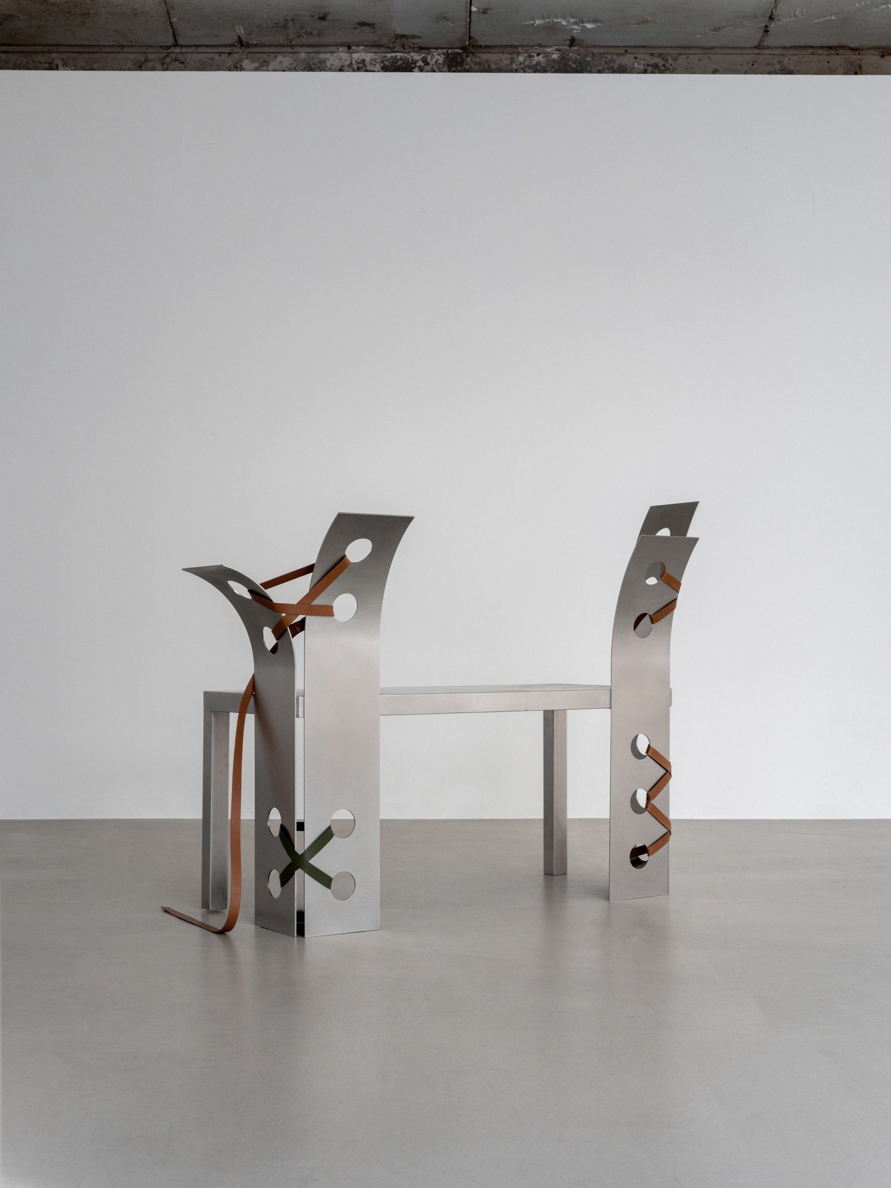 Pul Collection by Nara Lee, photographed by Namuk Kim — A bench with curved steel uprights and tan leather lacing seen from a three-quarter angle, the bowing backrest showing the steel flex.