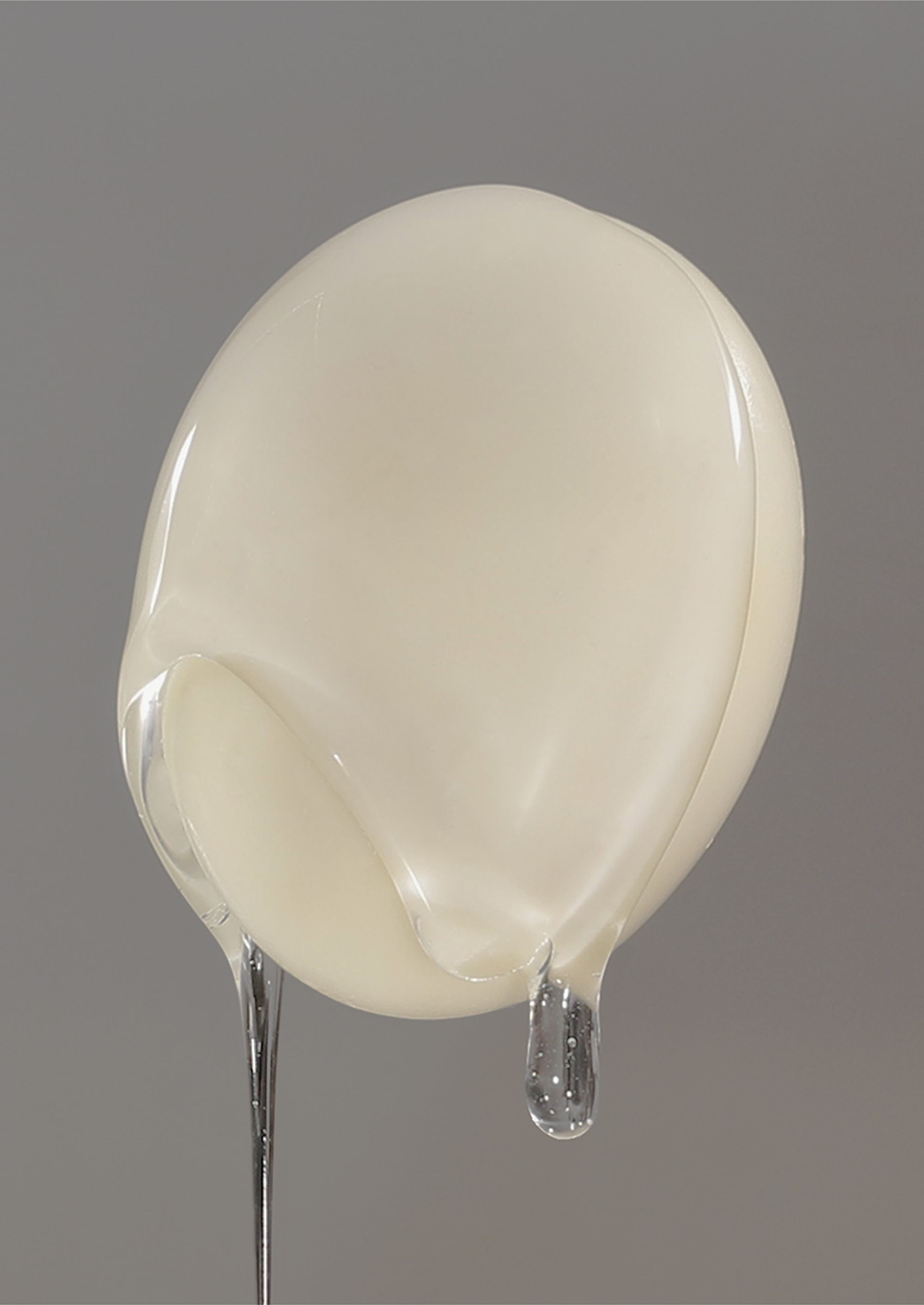 Trust Me by Jinyong Lian, photographed by Jinyong Lian — A translucent milky balloon cast in the form of a human face, mounted on two steel pins, beginning to drip clear liquid.