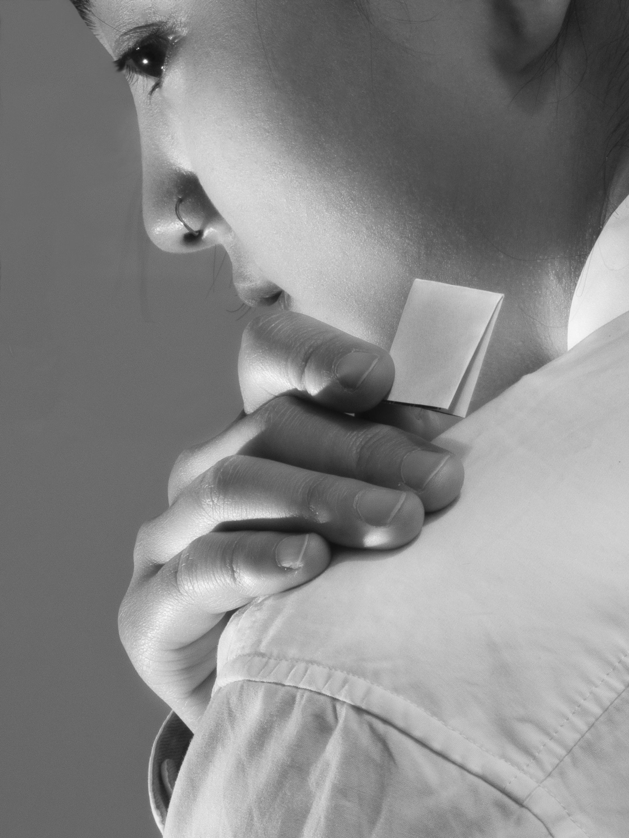 Trust Me by Jinyong Lian, photographed by Jinyong Lian — Black-and-white close crop of a face in profile, one hand cradling the jaw, a white adhesive patch at the collarbone.