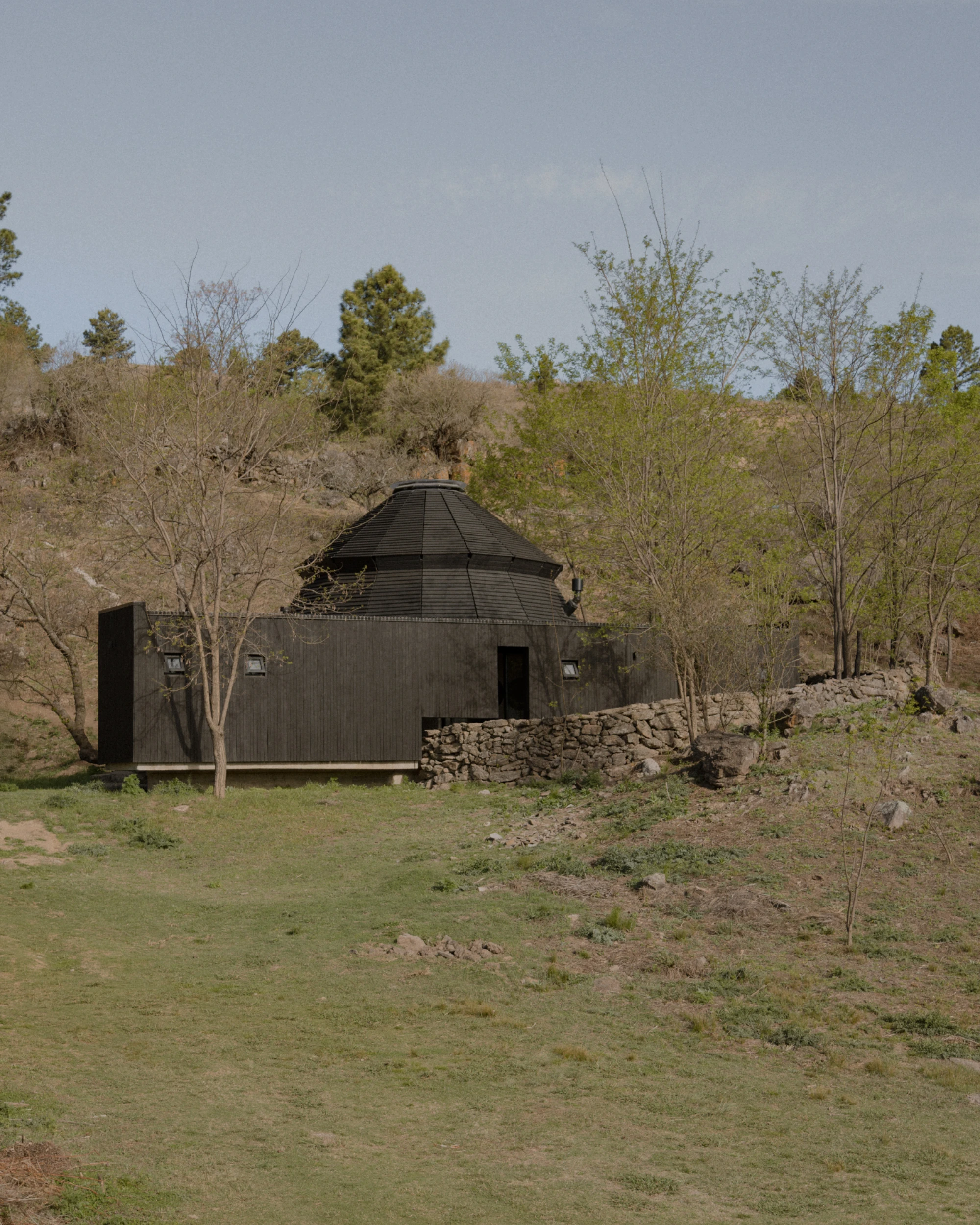 Pavilion El Durazno by Nicolás Oks: a 70 m² charred-timber pavilion folded into a Sierras landscape of Jesuit stone walls and molle trees.