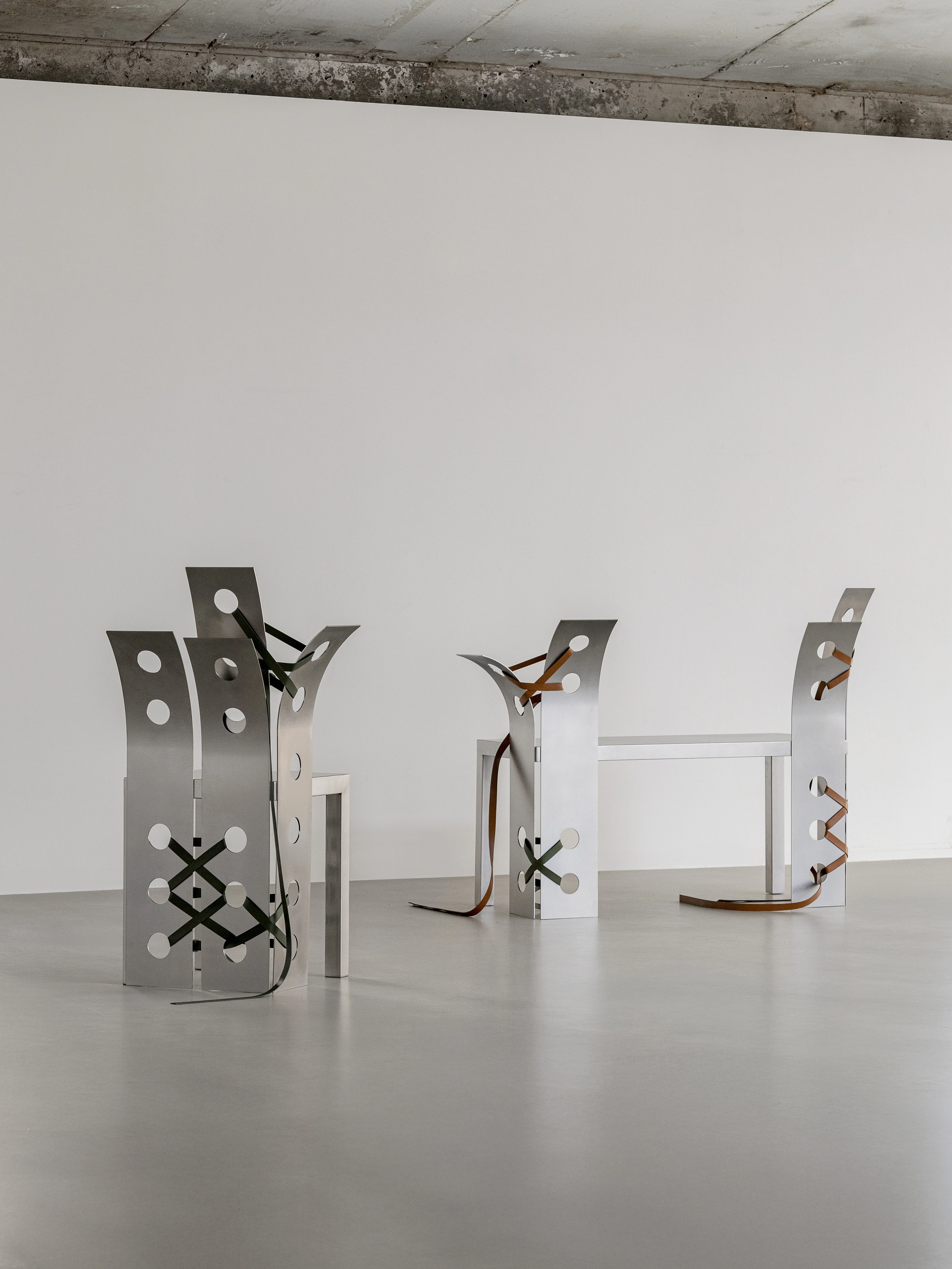 Pul Collection by Nara Lee, photographed by Namuk Kim — Three stainless-steel chairs with punched circular holes and leather cross-lacing stand in an open window-lit space.