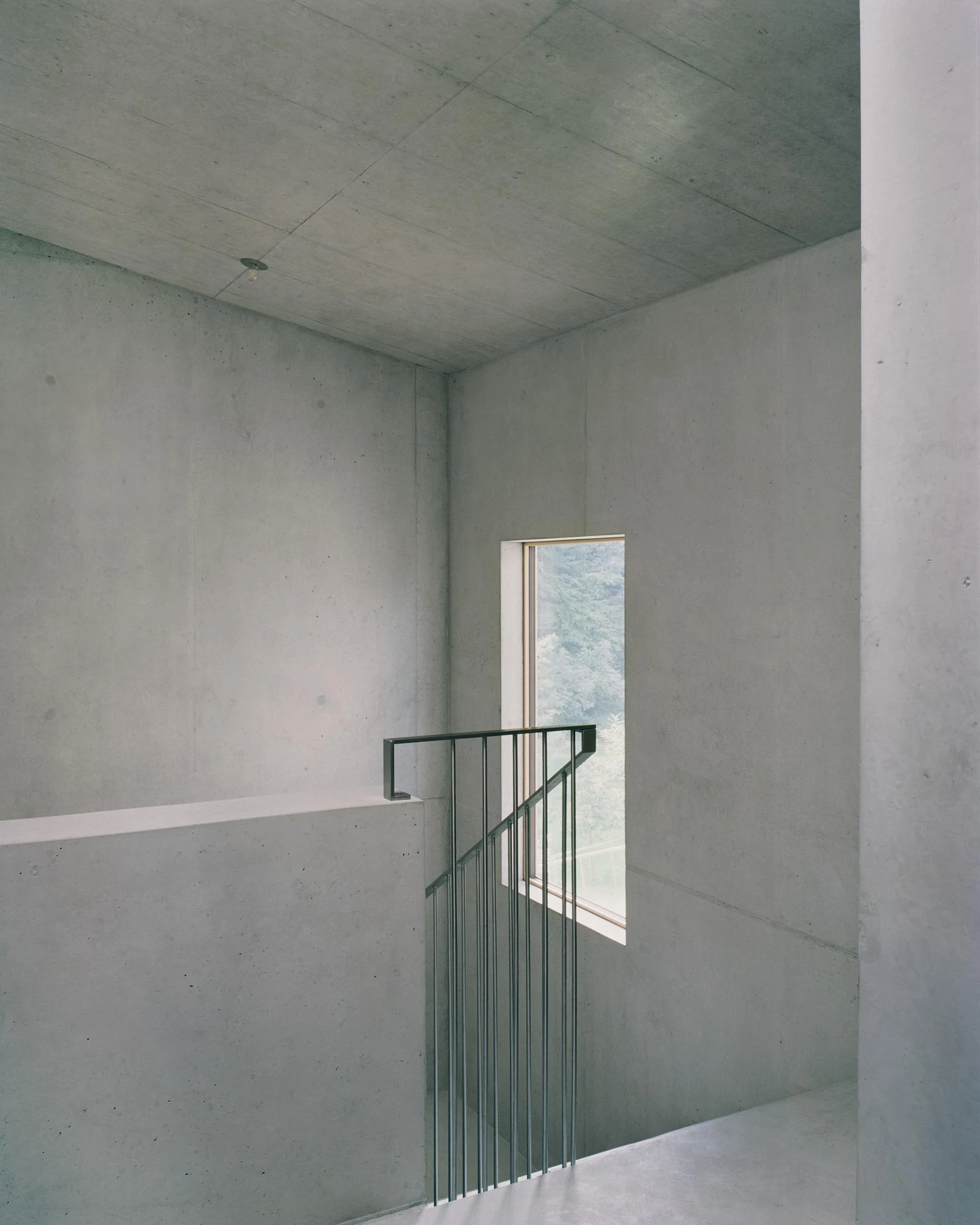 Hameau des Marais by Deschenaux Architectes, photographed by Rory Gardiner — Interior concrete staircore: board-formed walls and ceiling, a steel tubular balustrade, a slim timber-framed window throwing a blade of light across the upper landing.