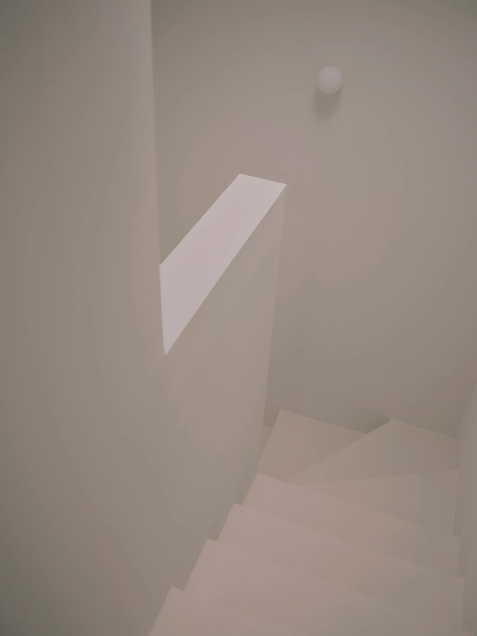 Casa St-Maximale by Maximale, photographed by David Zarzoso — Looking down the uppermost stair from above, the white plastered stairwell revealing a diagonal shaft of skylight across the wall and the microcement treads descending into the lower landing.