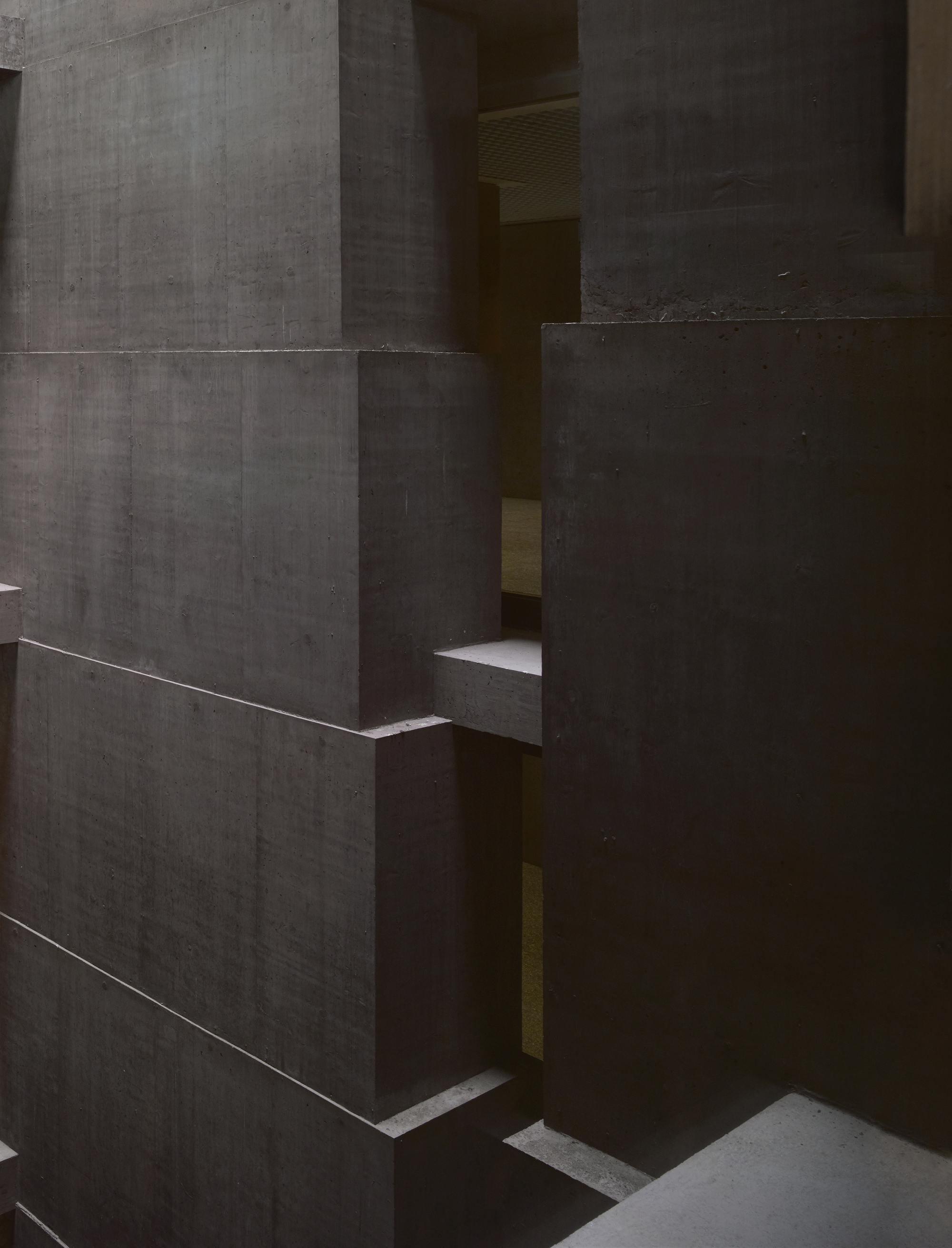 Baloise Insurance Company Office Tower by Valerio Olgiati, photographed by Bas Princen — Interior stair passage between massive concrete volumes, narrow slots of warm light visible through gaps in the brown-grey walls.