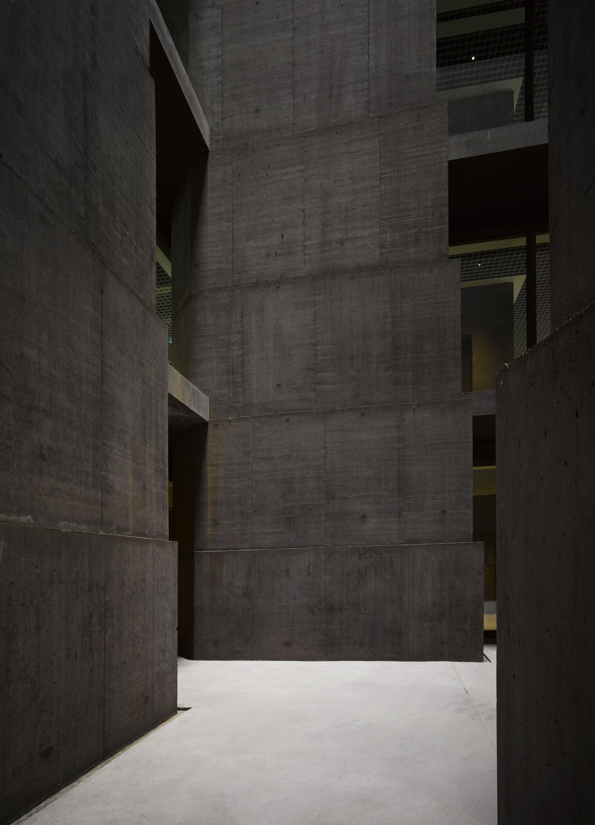 Baloise Insurance Company Office Tower by Valerio Olgiati, photographed by Bas Princen — Ground-level passage forms a canyon between smooth concrete walls, daylight filtering down from the void above.