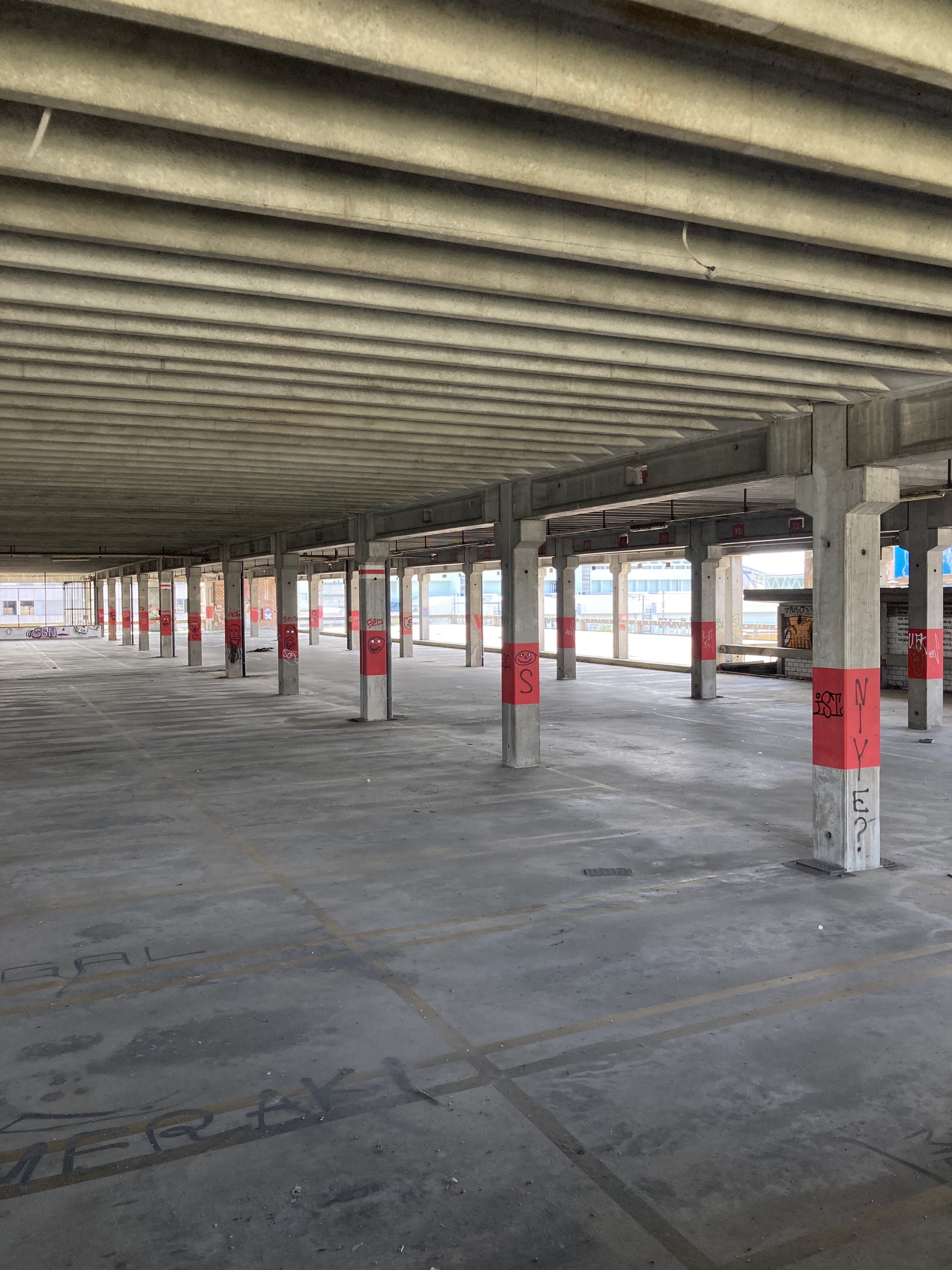 Elementa — Walkeweg Housing Development by Parabase, photographed by Parabase — Interior of the Lysbüchel parking garage before deconstruction, ribbed ceiling panels spanning between columns with faded red bands, raw concrete floor below.