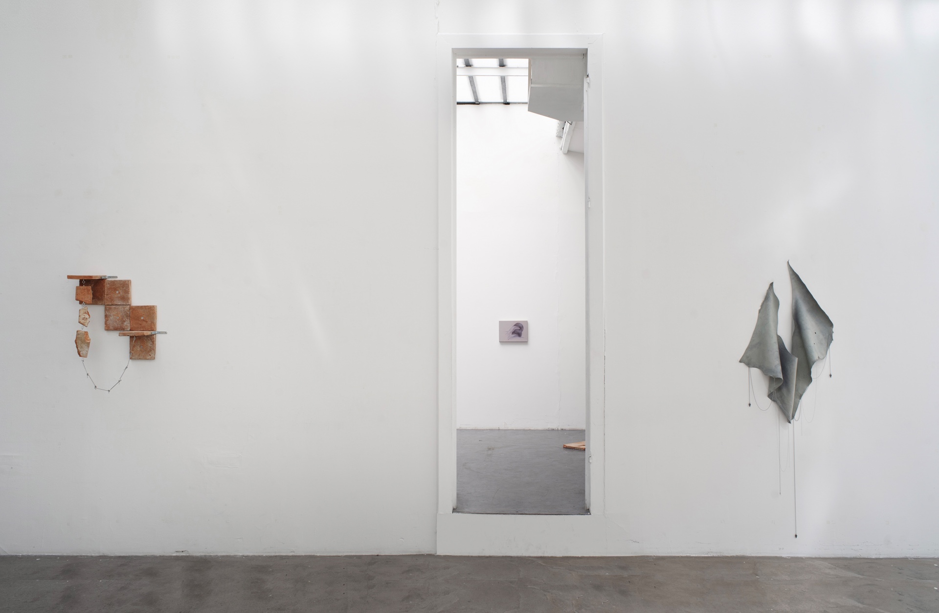 Main de fer, gant de velours by Agurto + Fiedler, photographed by Katherinne Fiedler — Exhibition view through doorway, Bedrock at left, small oil painting above threshold, Humedal leather and chains at right.