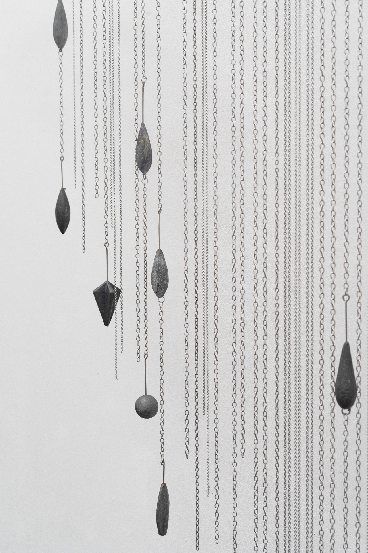 Main de fer, gant de velours by Agurto + Fiedler, photographed by Katherinne Fiedler — Garúa detail, lead plumb bobs in teardrop and geometric forms suspended on fine chains against white wall.