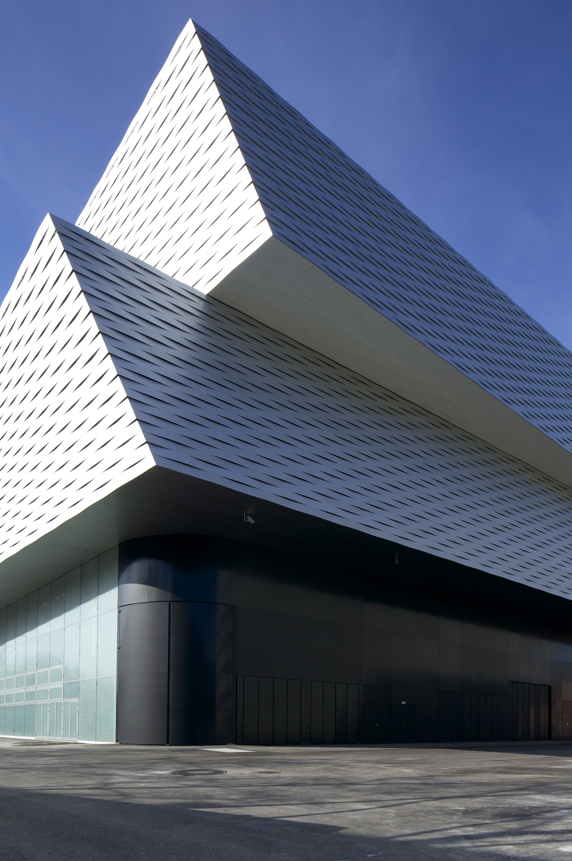 Messe Basel New Hall by Herzog & de Meuron, photographed by Messe Basel — Two offset exhibition volumes stack at the building corner, their aluminum skin appearing white against deep blue sky.