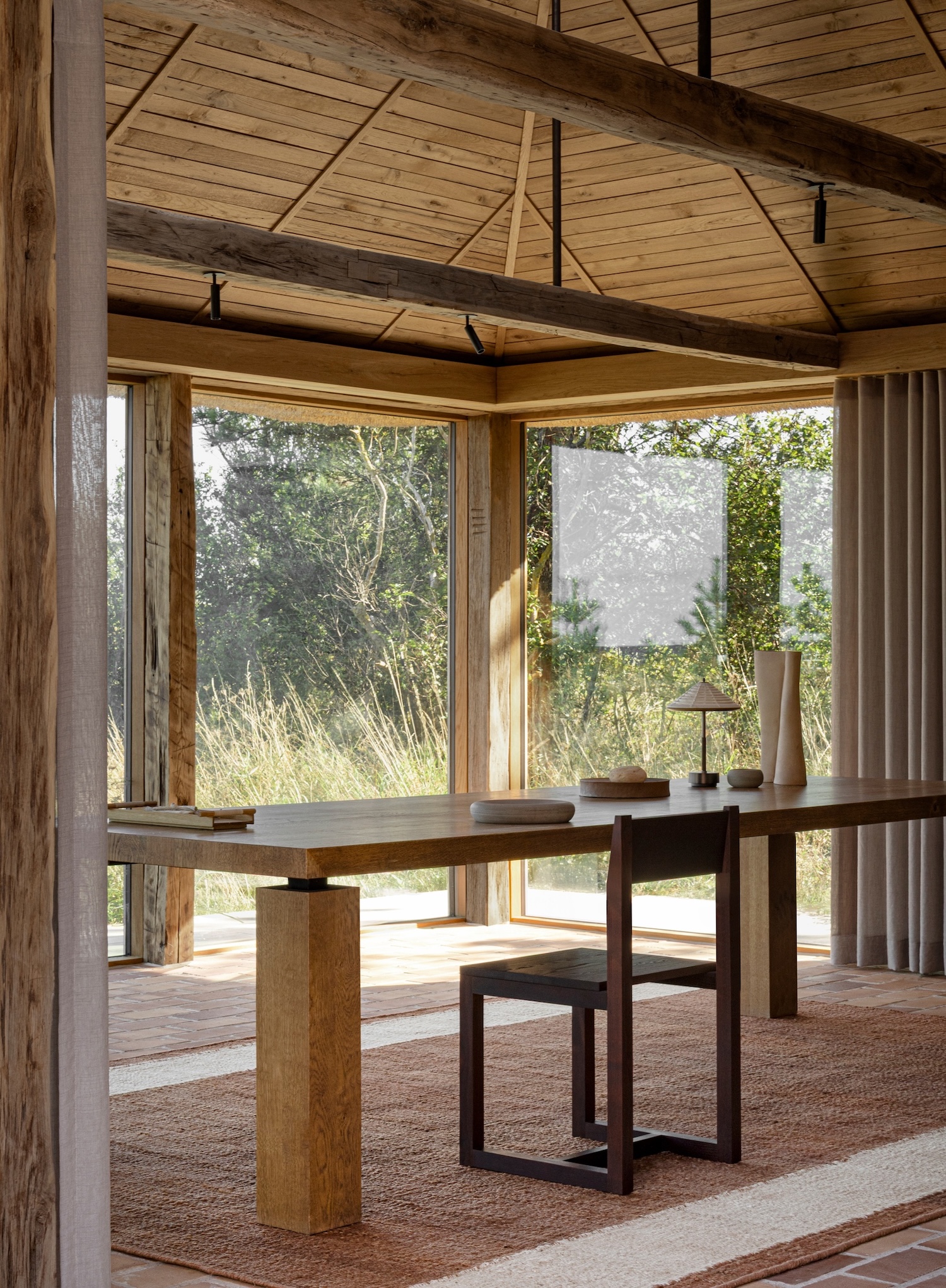 Shoreline Studio by Norm Architects, photographed by Norm Architects — Desk workspace with Frama Chair 01 in dark wood, cylindrical oak leg table, corner windows opening to coastal grasses with sheer curtain filter.