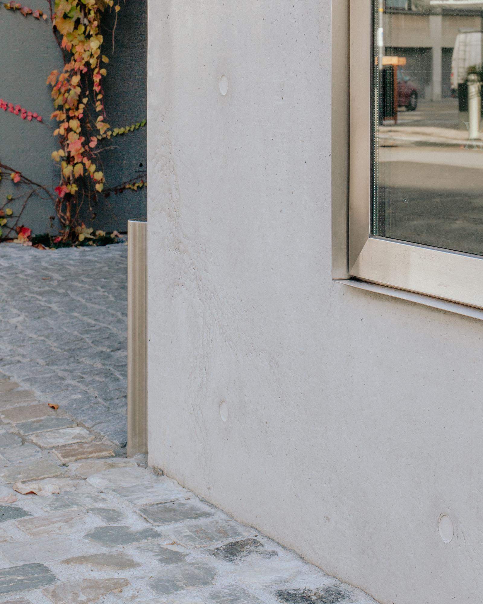 Xavier Hufkens Gallery by Robbrecht en Daem Architecten, photographed by Jeremy Piret — Detail of fair-faced concrete corner meeting Belgian cobblestones, autumn vine on adjacent wall, stainless steel corner guard.
