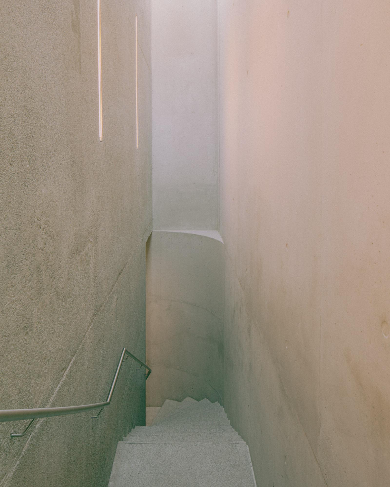 Xavier Hufkens Gallery by Robbrecht en Daem Architecten, photographed by Jeremy Piret — Narrow concrete stair corridor between raw cast walls, stainless handrail, vertical LED strip lighting.