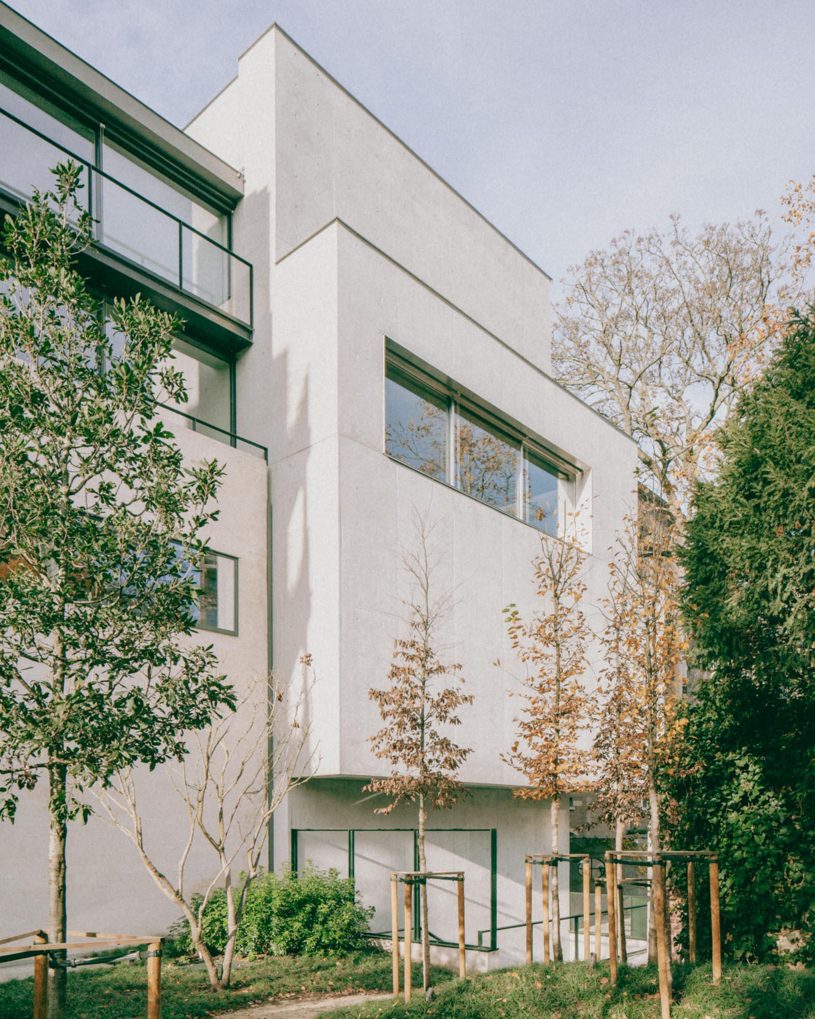 Xavier Hufkens Gallery by Robbrecht en Daem Architecten, photographed by Jeremy Piret — Garden elevation showing staggered white volumes with ribbon windows, young trees in foreground, diffused afternoon light.