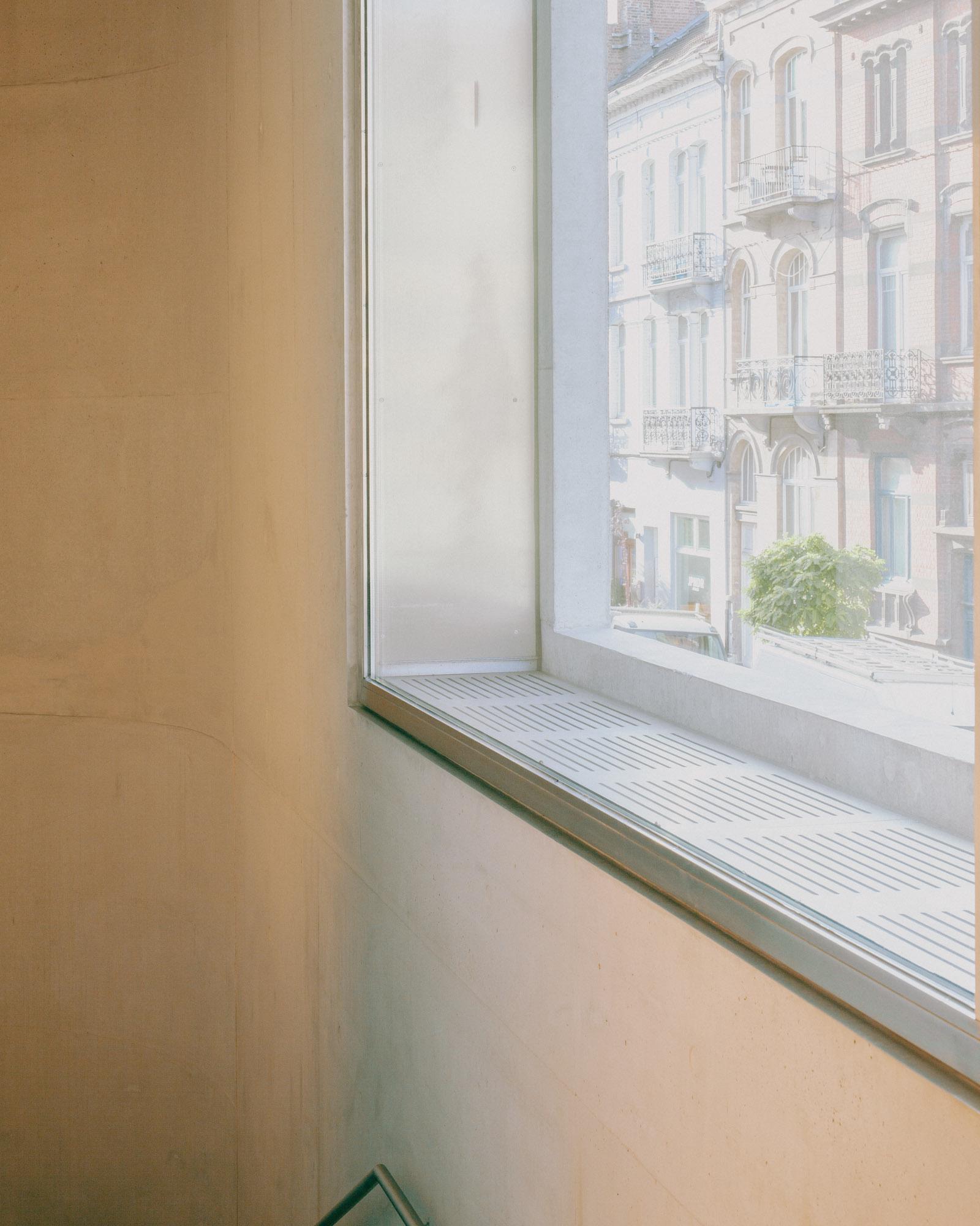 Xavier Hufkens Gallery by Robbrecht en Daem Architecten, photographed by Jeremy Piret — Window detail framing ornate Brussels townhouse facades, concrete wall with faint formwork lines, metal sill.