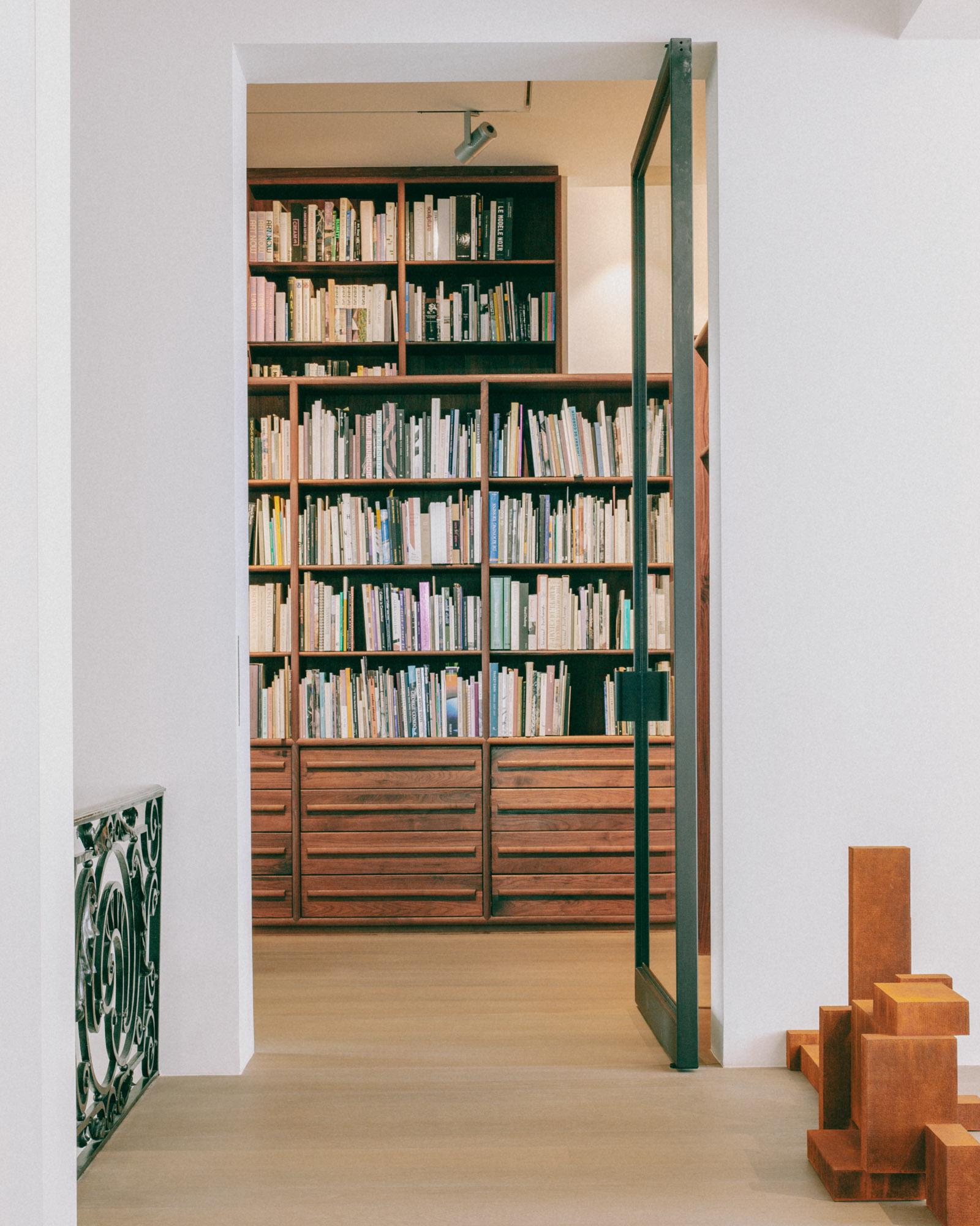 Xavier Hufkens Gallery by Robbrecht en Daem Architecten, photographed by Jeremy Piret — Threshold from new to old: walnut bookshelf library visible through doorway, ornate radiator grille, corten sculpture fragment at right.
