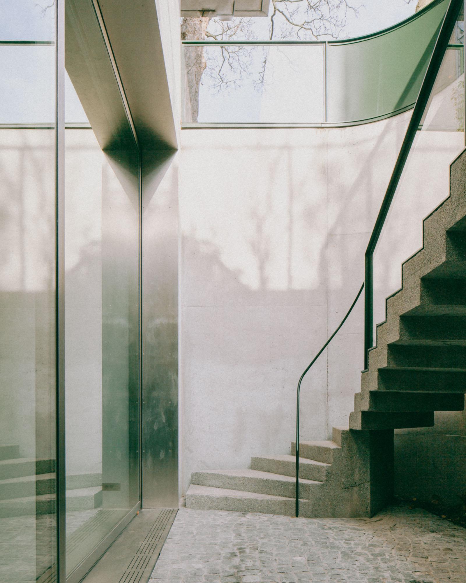 Xavier Hufkens Gallery by Robbrecht en Daem Architecten, photographed by Jeremy Piret — External stair with curved glass balustrade, tree branch shadows cast across concrete walls, diffused skylight.