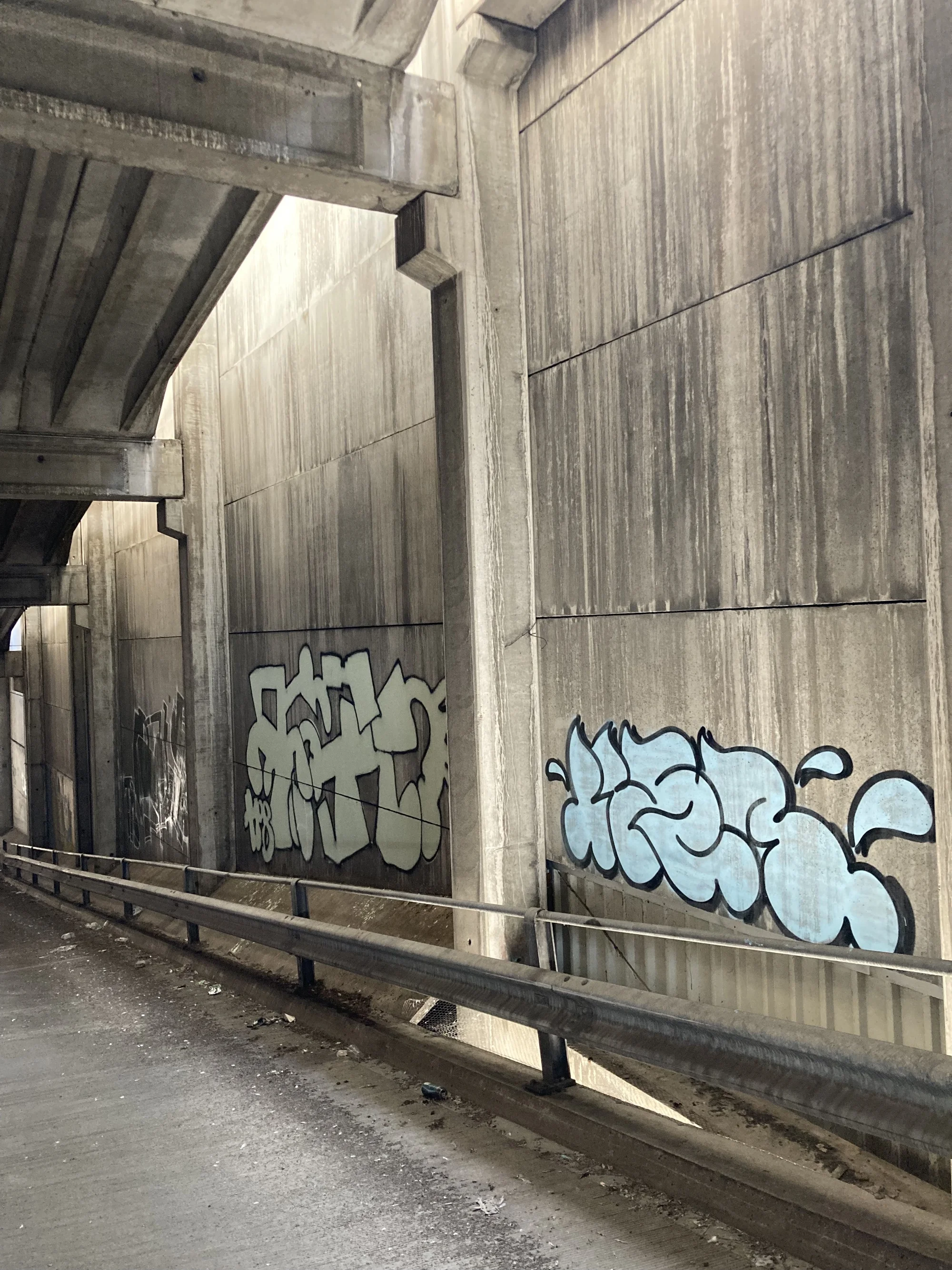 Elementa — Walkeweg Housing Development by Parabase, photographed by Parabase — Weathered precast wall panels of the donor parking garage, graffiti tags in white and blue, ribbed soffit visible at the edge of frame, metal guardrail at bottom.