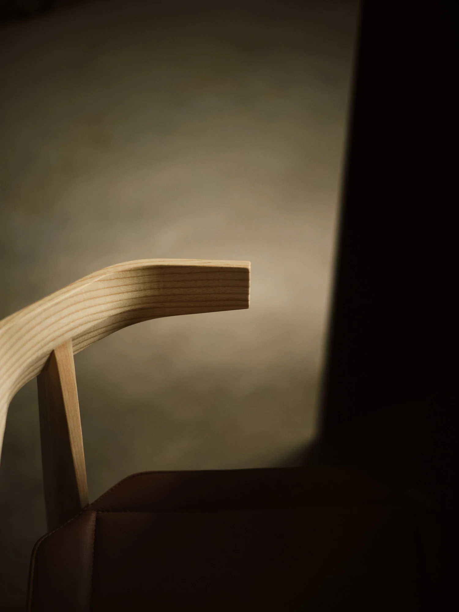 Rasa Collection by Carlos Pereira, photographed by Paulo Carvalho — Oblique close view of two natural ash Rasa chairs: the grain pattern of the seat shell and curved backrest are visible in parallel lines under the raking warehouse light.