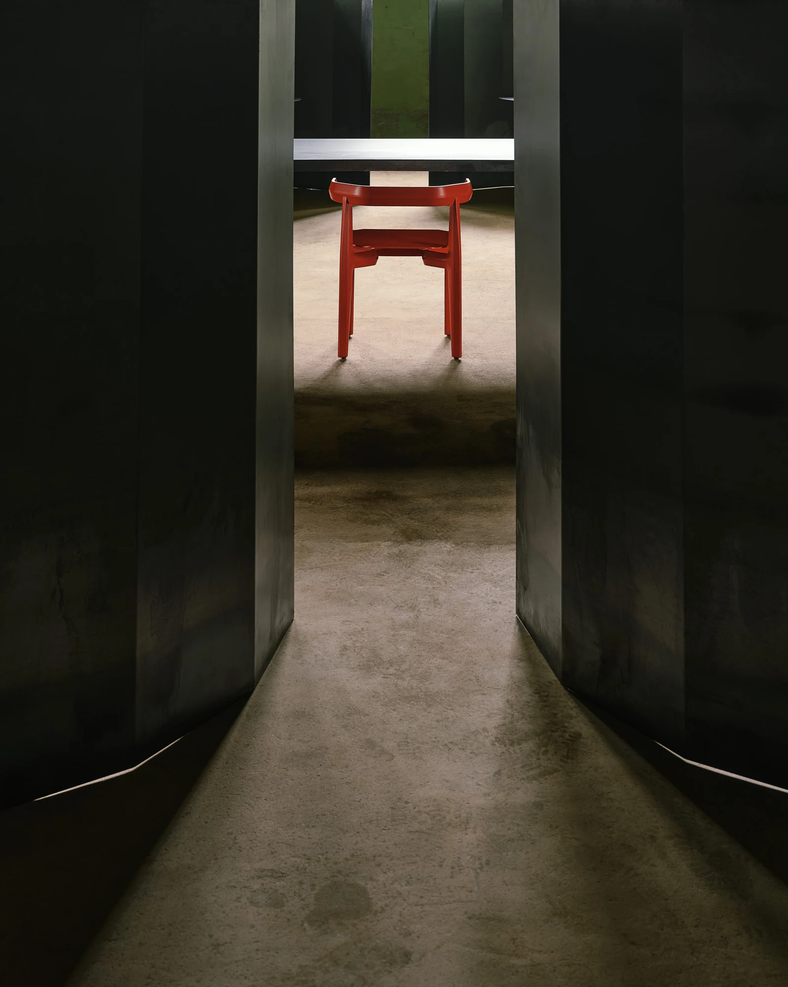 Rasa Collection by Carlos Pereira, photographed by Paulo Carvalho — A red lacquered Rasa chair is framed between two dark steel partition panels in the warehouse: the chair reads as a colour point at the end of a narrow corridor, the concrete floor…
