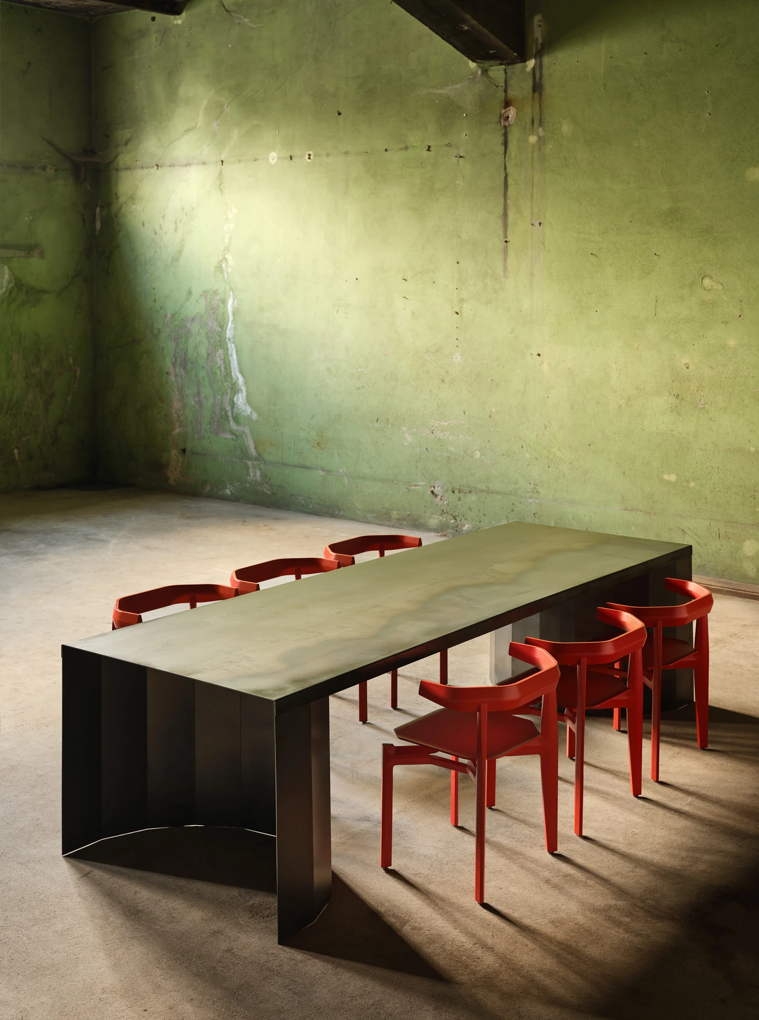 Rasa Collection by Carlos Pereira, photographed by Paulo Carvalho — Natural ash Rasa chairs with terracotta-toned seat cushions arranged in a row along a dark steel partition, the warehouse light falling obliquely across the seats.