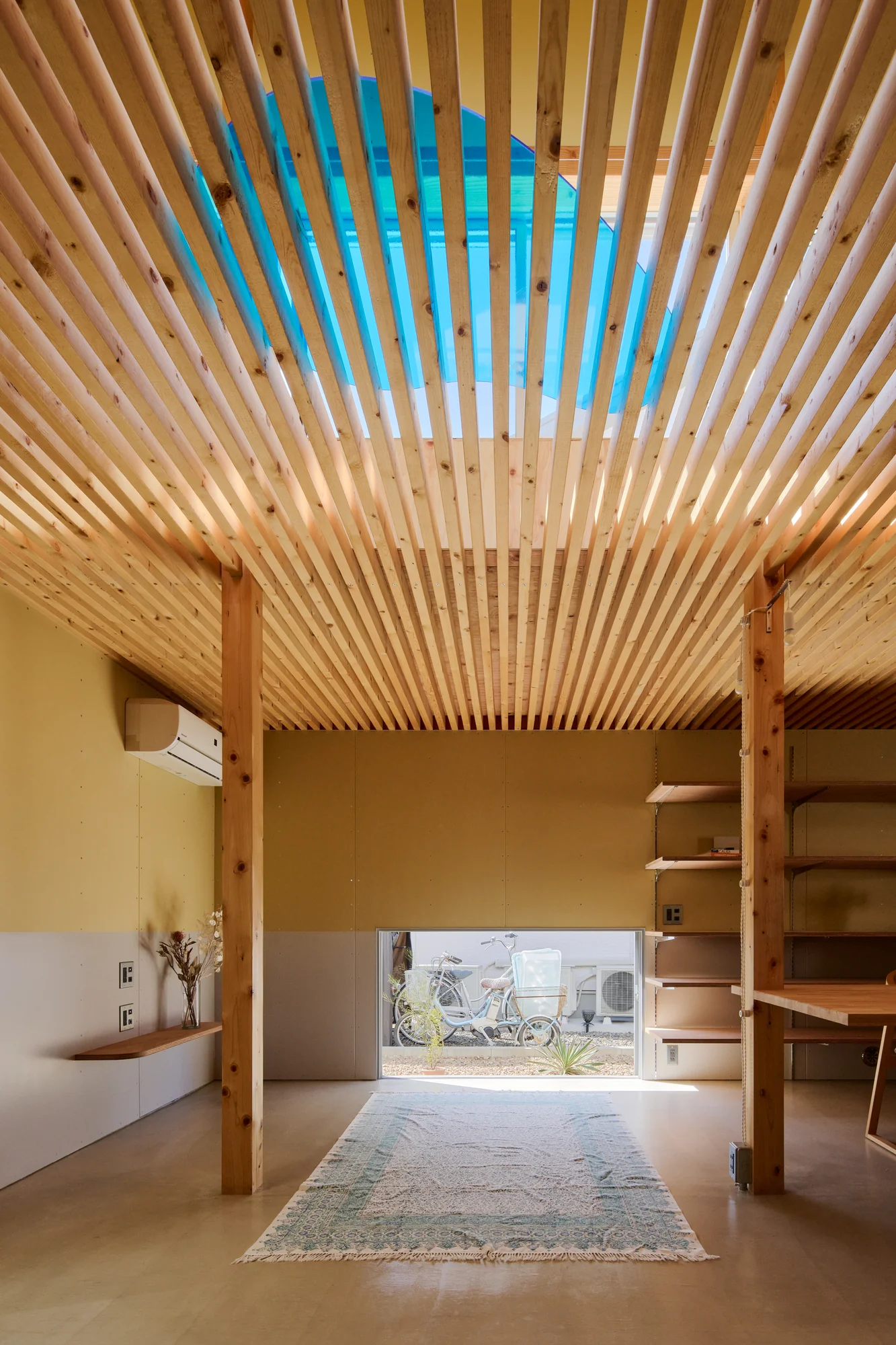 House TN by 1-1 Architects, photographed by Takashi Uemura — Light passes through the louver ceiling as striped bands, illuminating the earthen floor and timber columns in the ground-floor living space.