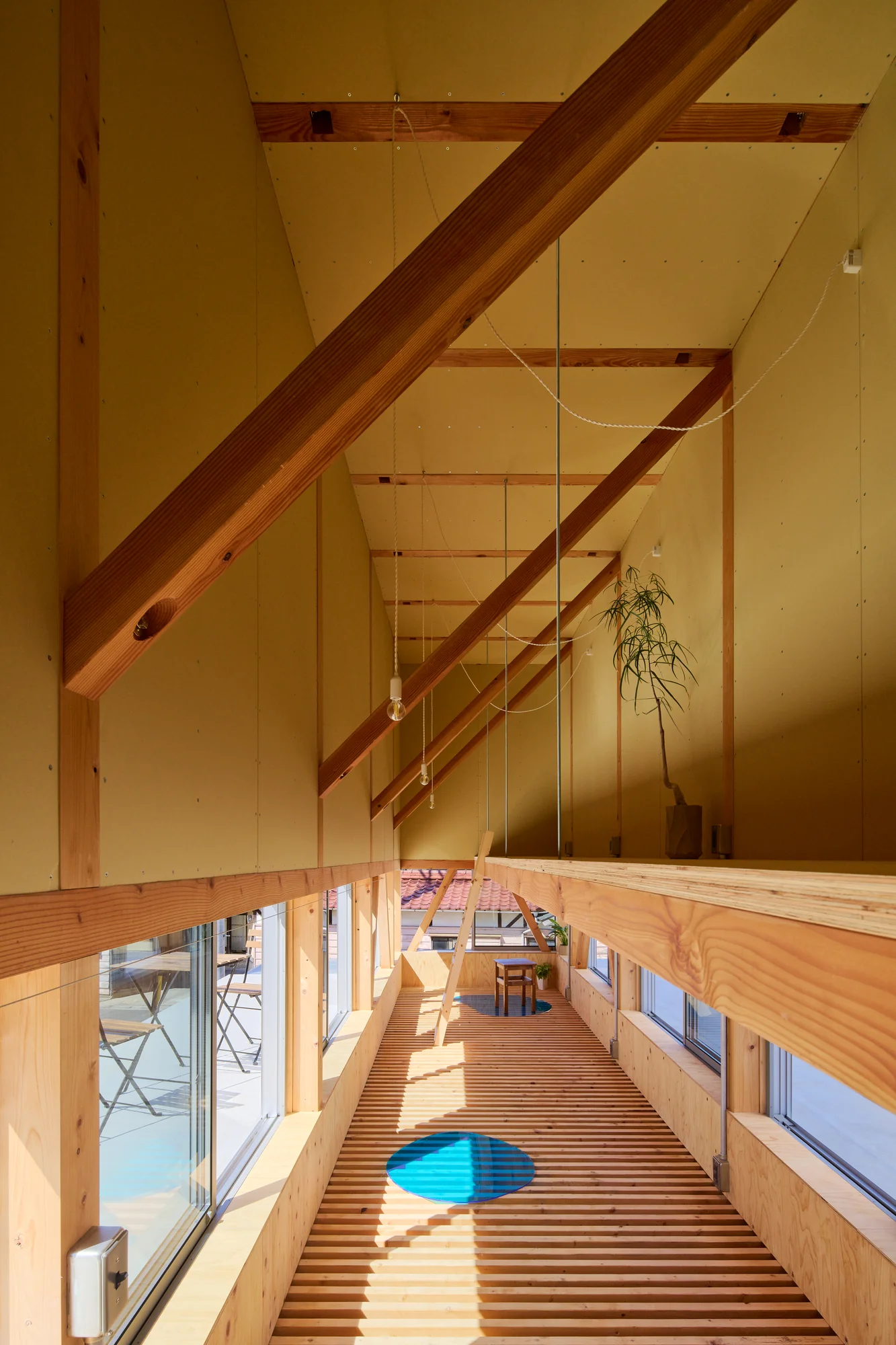House TN by 1-1 Architects, photographed by Takashi Uemura — Long view through the second floor—timber beams and diagonal braces frame the louver floor, terrace and hanging plant visible at the corridor's end.