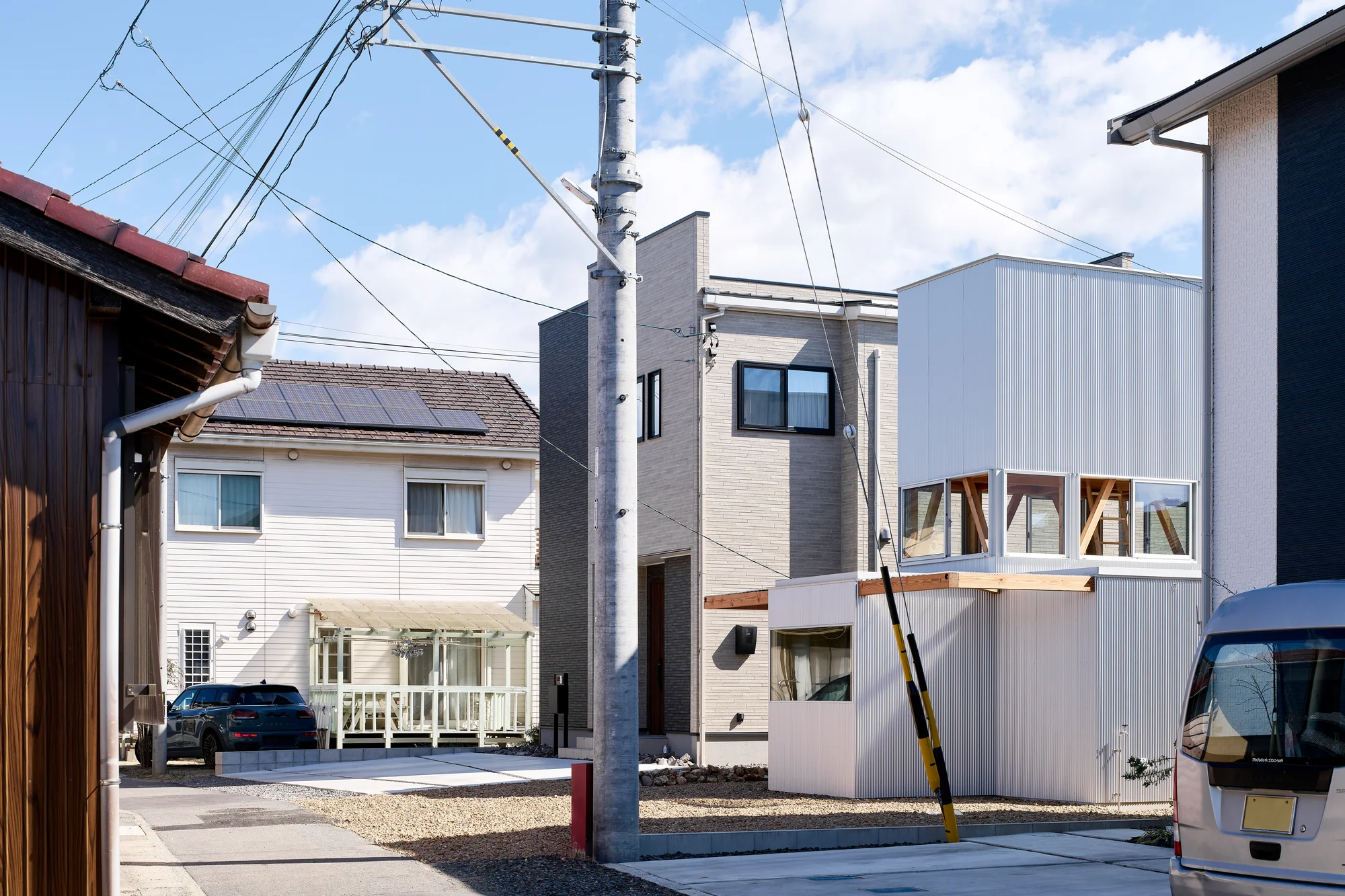 House TN by 1-1 Architects, photographed by Takashi Uemura — From the street, the house sits between neighboring volumes, its white corrugated cladding and exposed timber terrace beam distinguishing it from adjacent structures.