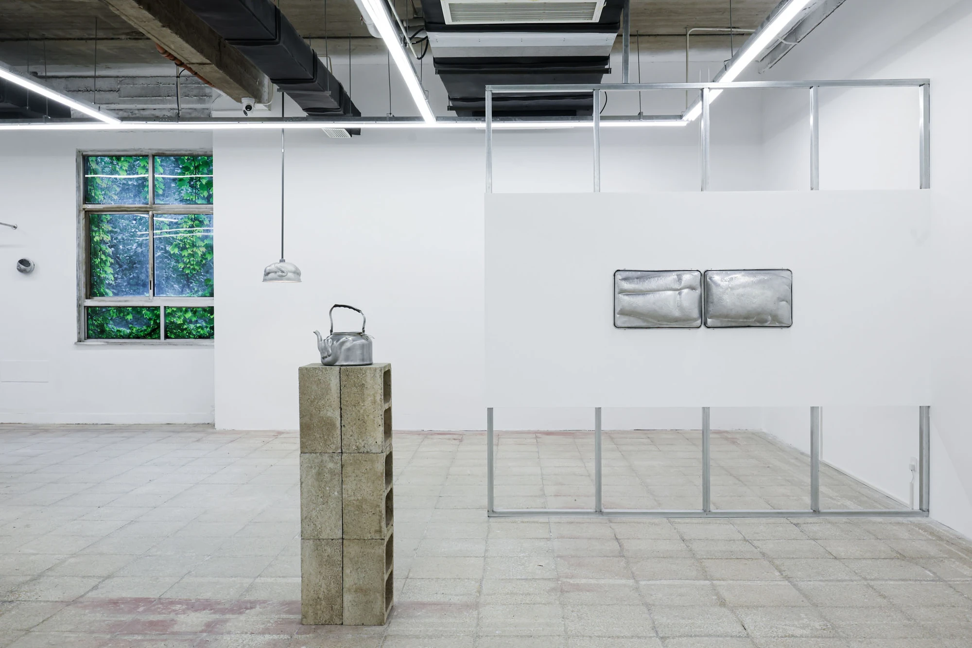 A User Guide by Tian Jianxin, photographed at Capsule — installation view with an aluminium kettle on stacked cinder blocks, a hammered dome lamp, and two tray-bound torsos mounted on a partition wall.