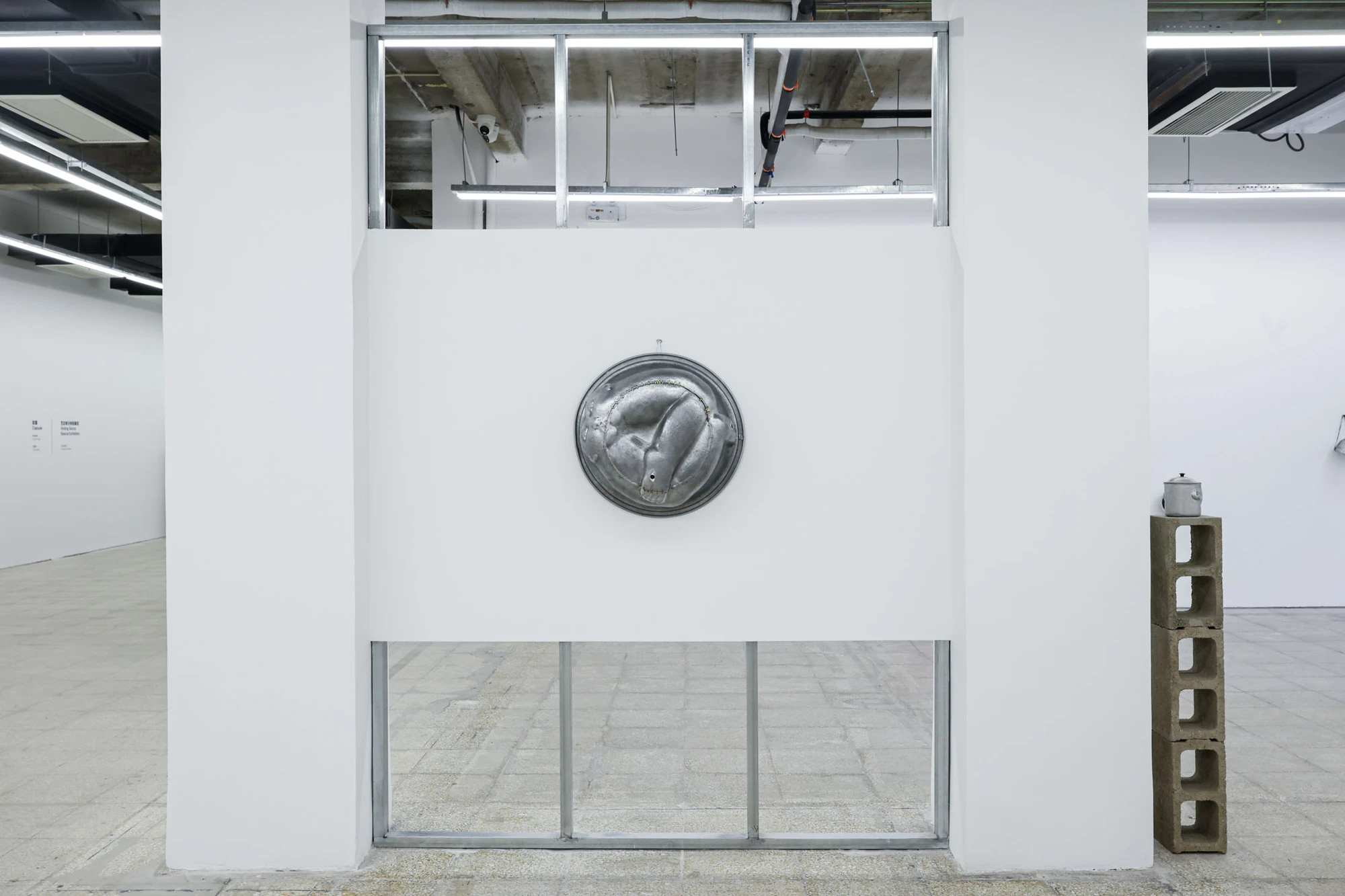 A User Guide by Tian Jianxin, photographed at Capsule — a hammered pendant lamp hangs above a flat relief, a video monitor, and a kettle on a cinder-block stack in a quiet corner.