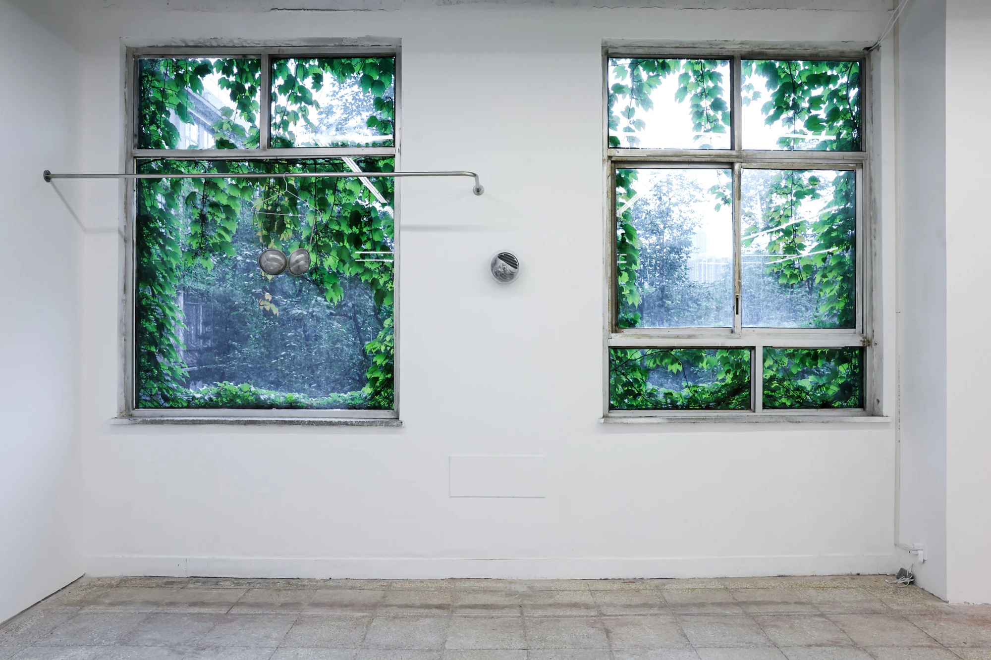 A User Guide by Tian Jianxin, photographed at Capsule — a single hammered aluminium fragment sits centered between two vine-covered windows like a face caught mid-blink.
