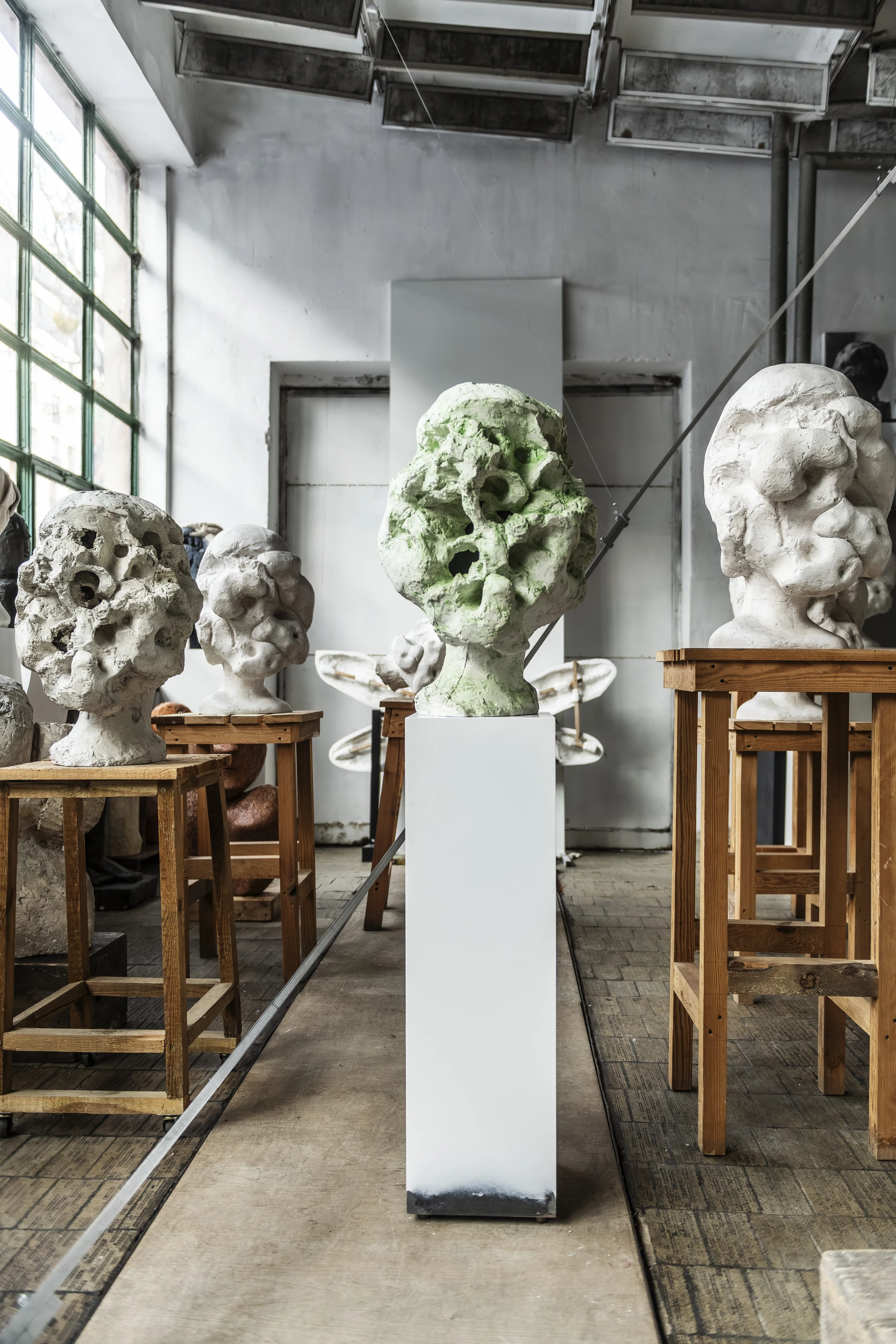 Magdalena Abakanowicz / Wanda Czełkowska by Abakanowicz Foundation, photographed by Norbert Piwowarczyk — three plaster head fragments set in front of a framed black-line drawing of a single head.