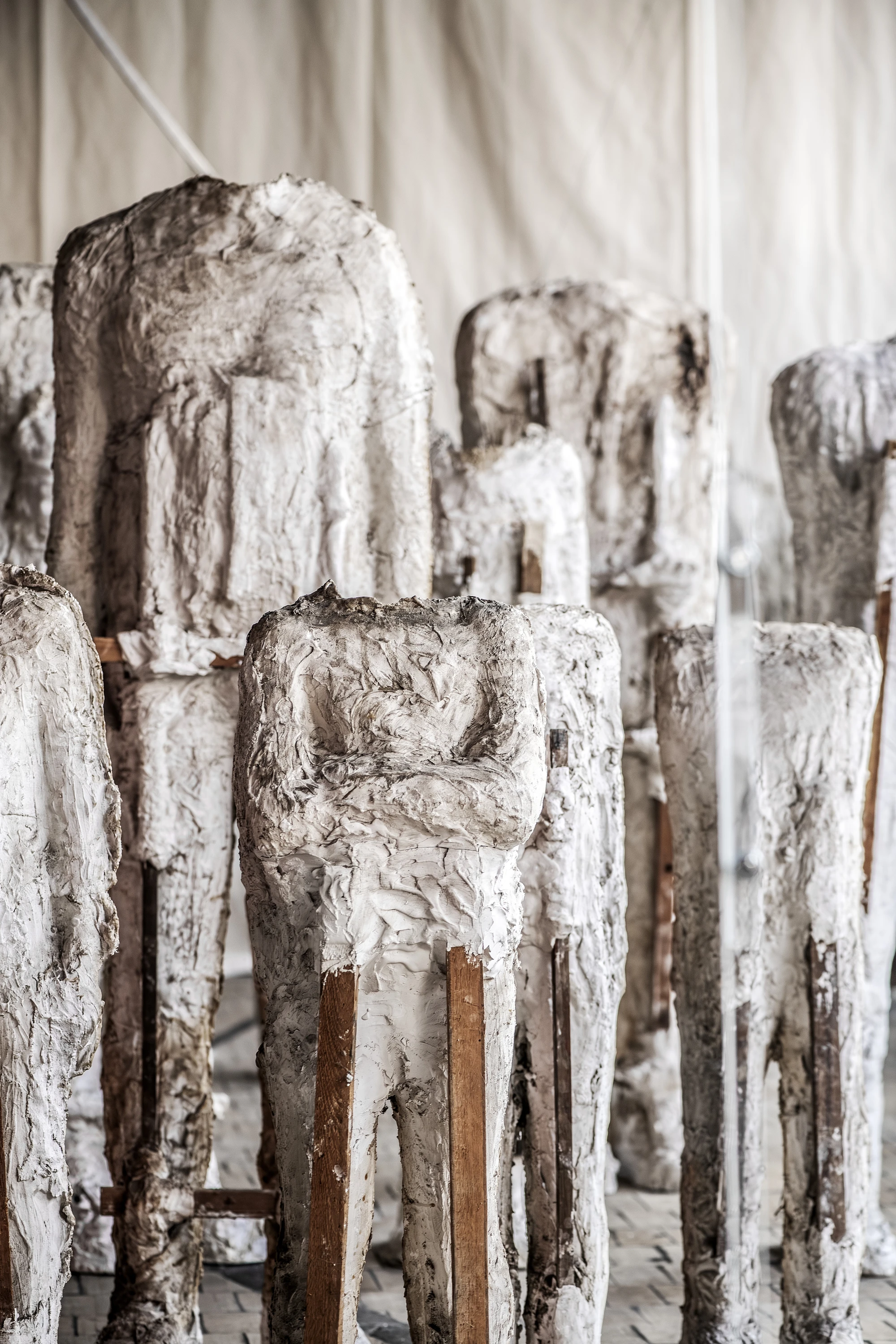 Magdalena Abakanowicz / Wanda Czełkowska by Abakanowicz Foundation, photographed by Norbert Piwowarczyk — knurled plaster heads on stools beneath a wall of black-and-white archival head photographs.