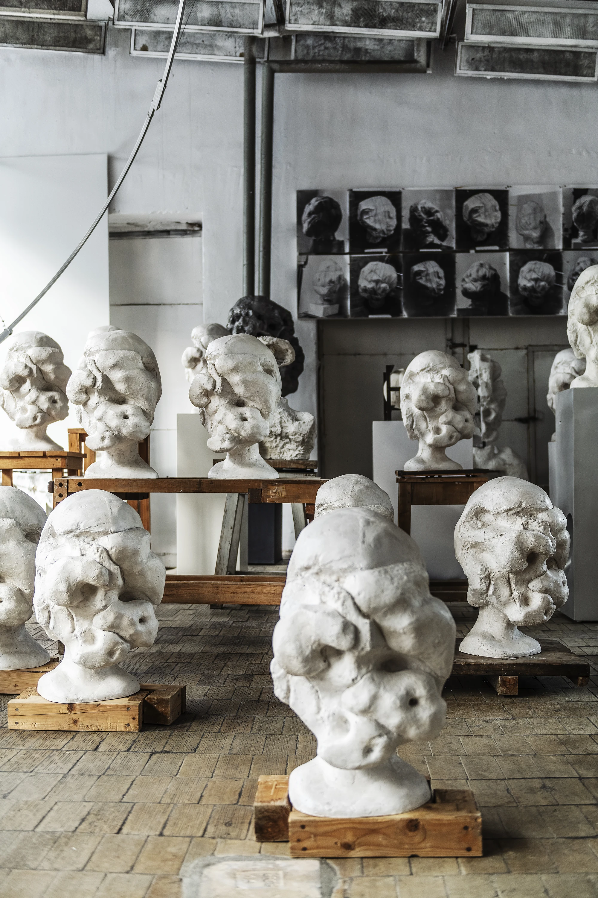 Magdalena Abakanowicz / Wanda Czełkowska by Abakanowicz Foundation, photographed by Norbert Piwowarczyk — daylight from a steel-framed window crossing two grouped plaster heads in the studio.