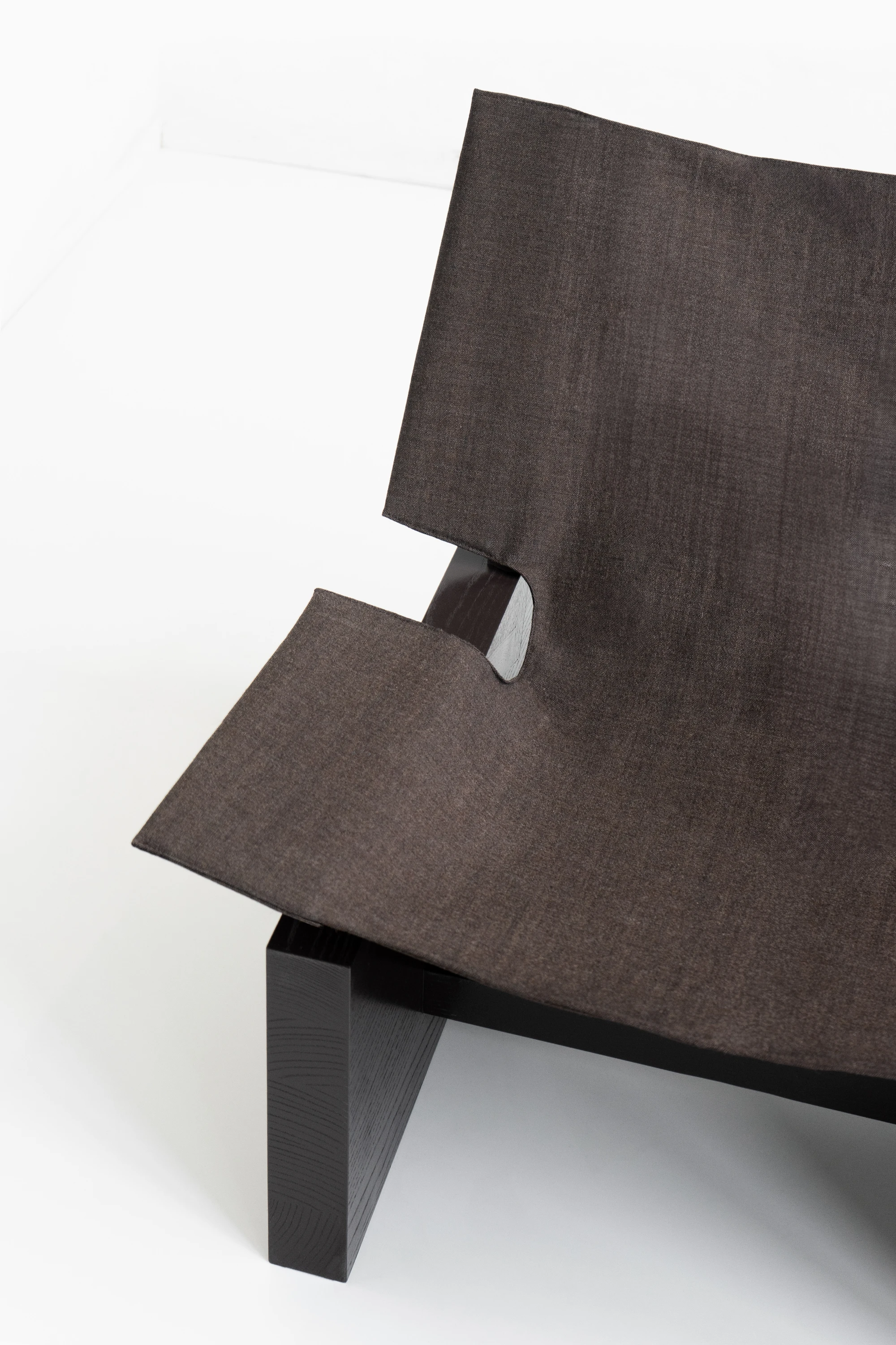 Suspens Lounge Chair by Perron et frères, photographed by Perron et frères — low-angle side view of the lacquered ash arm, backrest support, and visible grain through the dark finish.